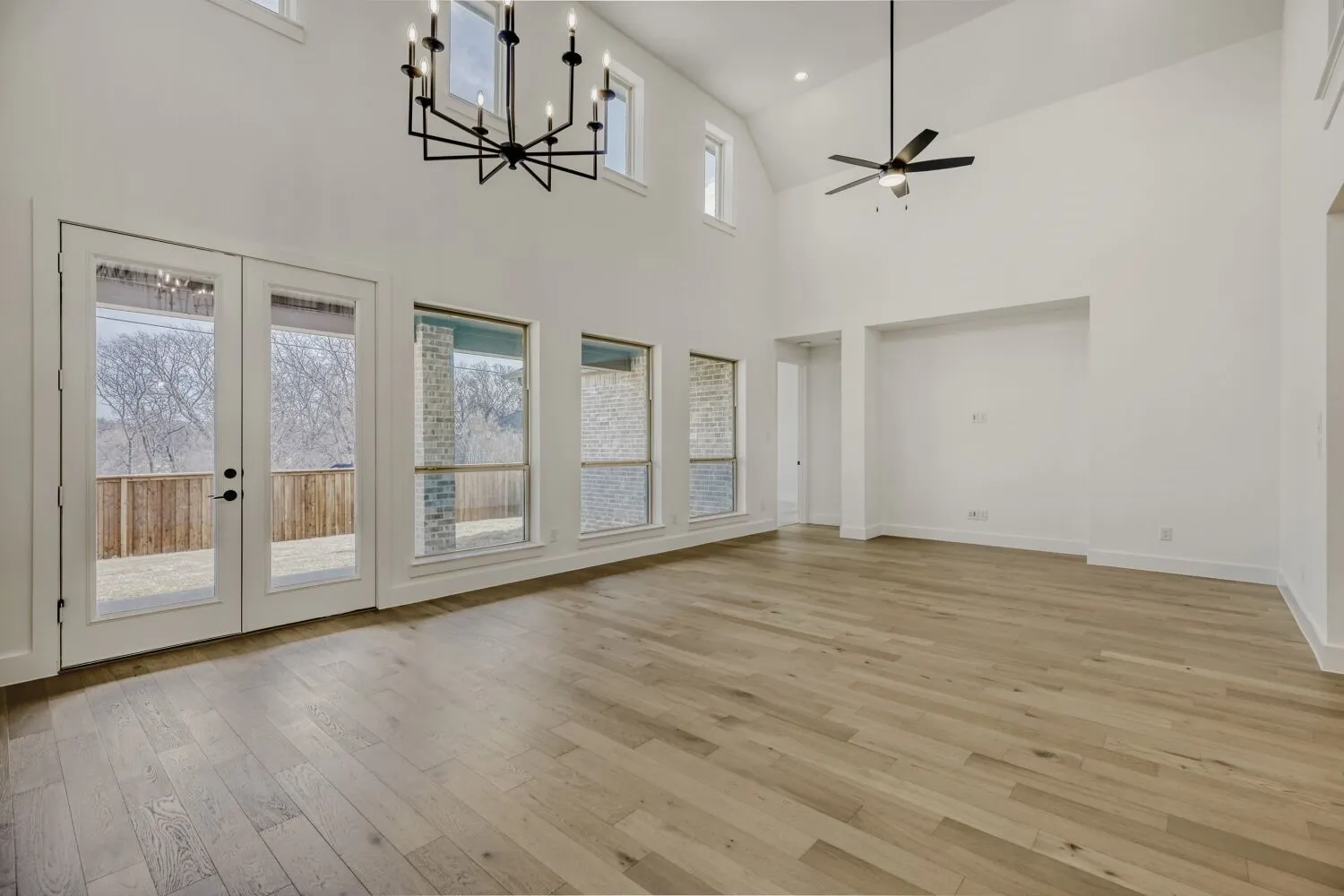 Unfurnished living room with hanging lights, light wood-type flooring, lofted ceiling, ceiling fan, and french doors