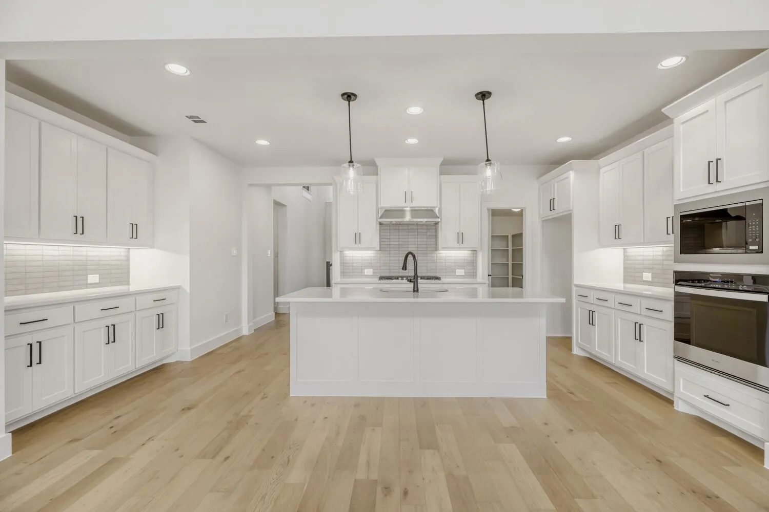 Kitchen featuring stainless steel appliances, hanging light fixtures, an island with sink, light wood finished floors, and white cabinets