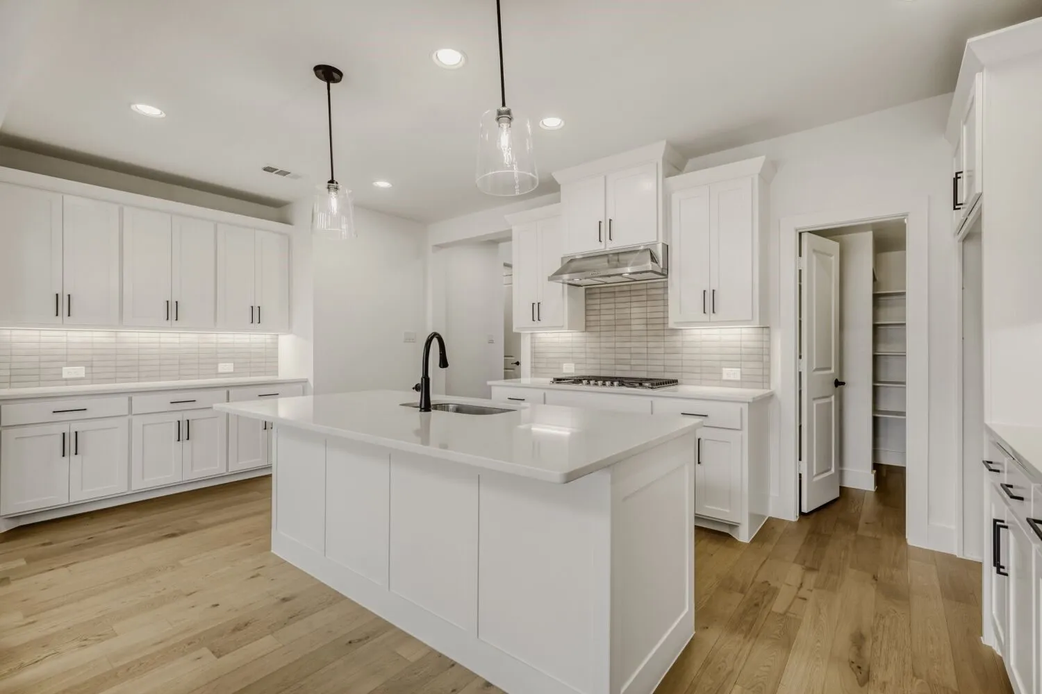 Kitchen featuring a center island with sink, light wood finished floors, hanging light fixtures, and white cabinetry