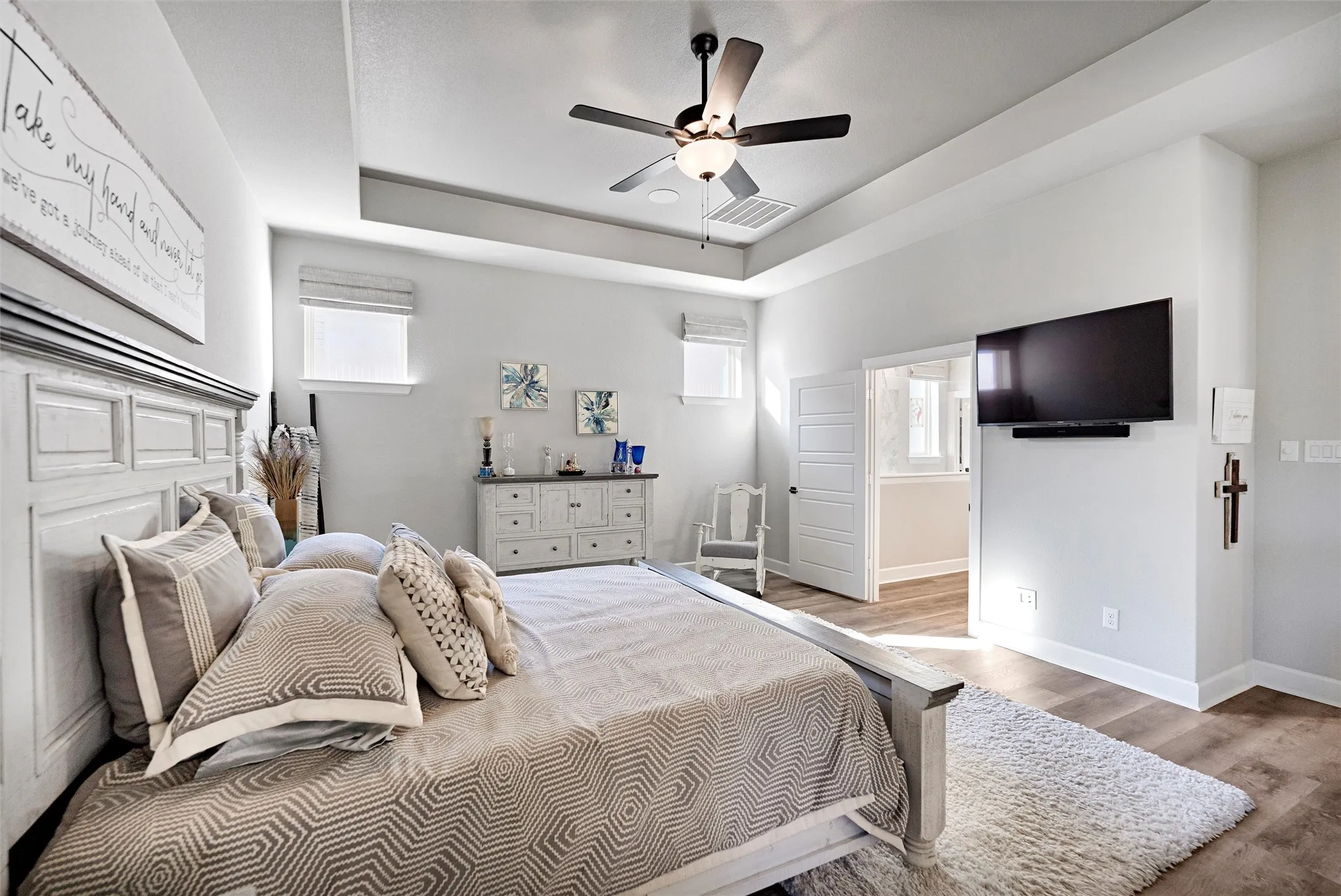 Bedroom featuring wood finished floors, a raised ceiling, and a ceiling fan