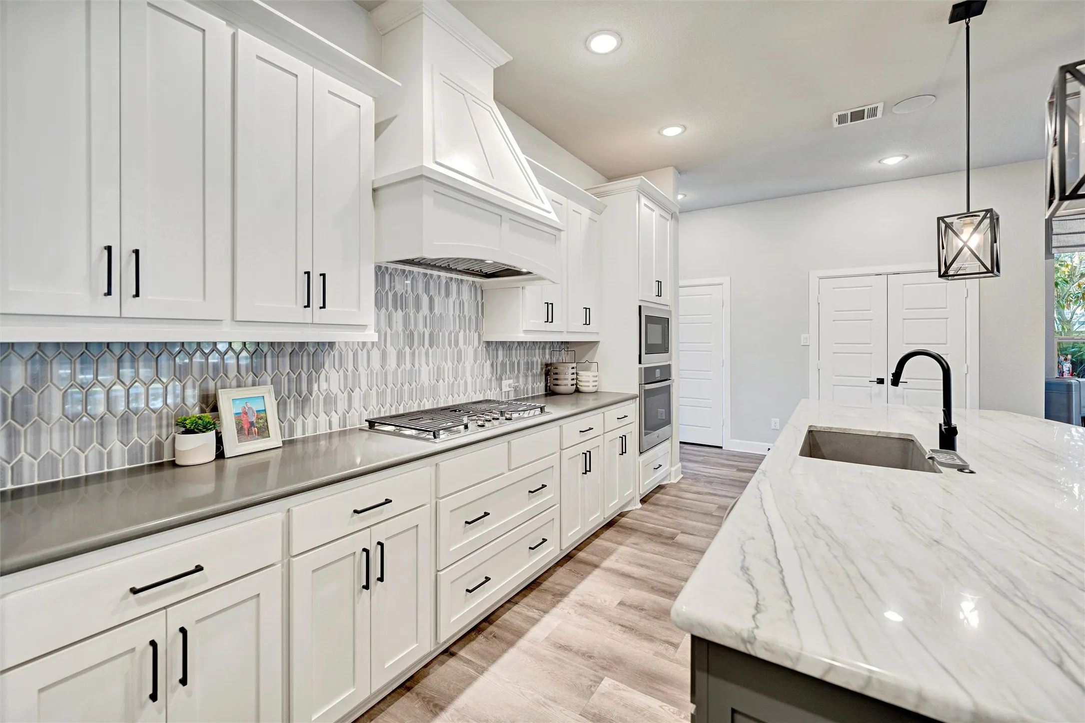 Kitchen with tasteful backsplash, decorative light fixtures, light wood-style floors, recessed lighting, and white cabinetry