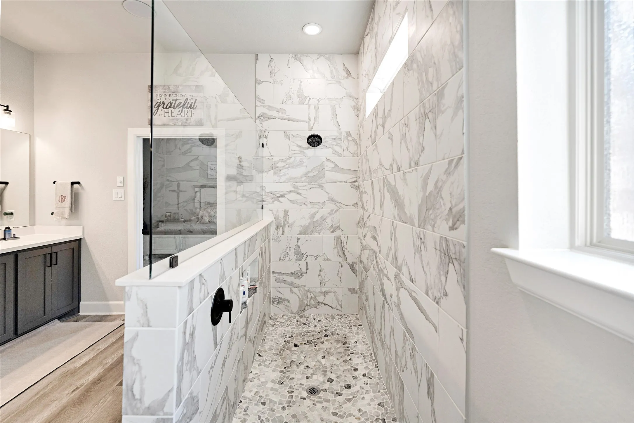 Bathroom with a marble finish shower, vanity, and light wood-style floors