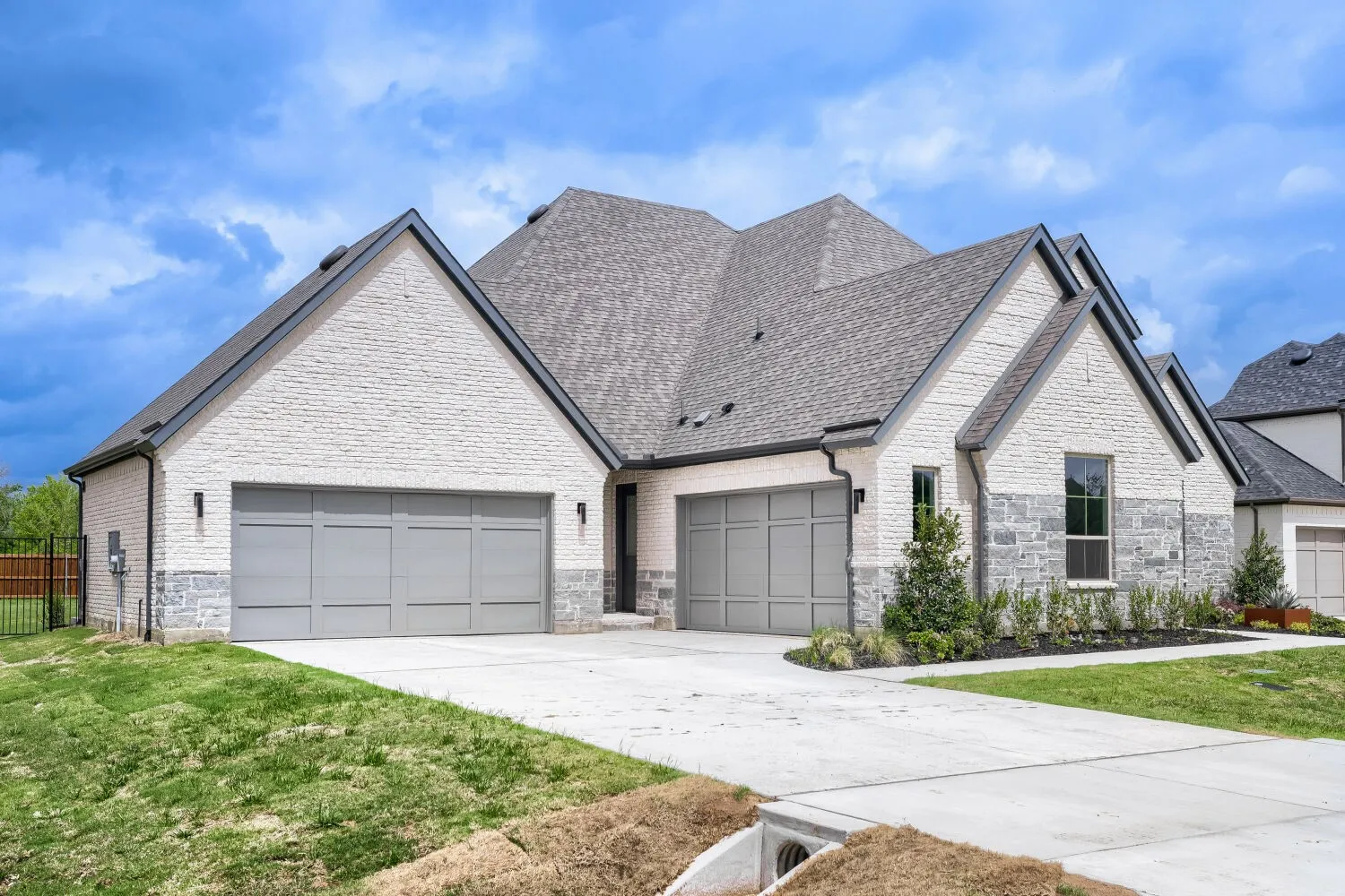 French country inspired facade with an attached garage, stone siding, concrete driveway, roof with shingles, and brick siding