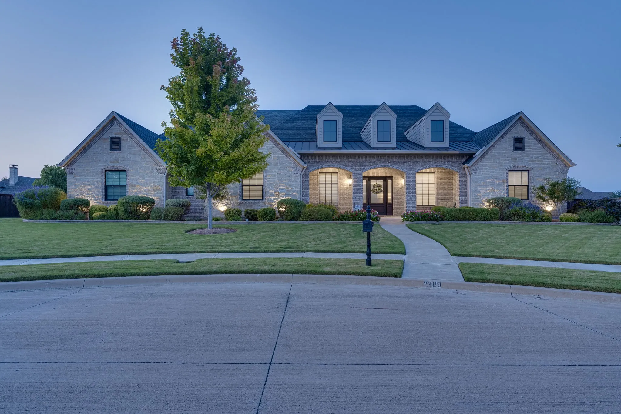 View of front facade featuring a lawn, covered porch, stone siding, and a standing seam roof
