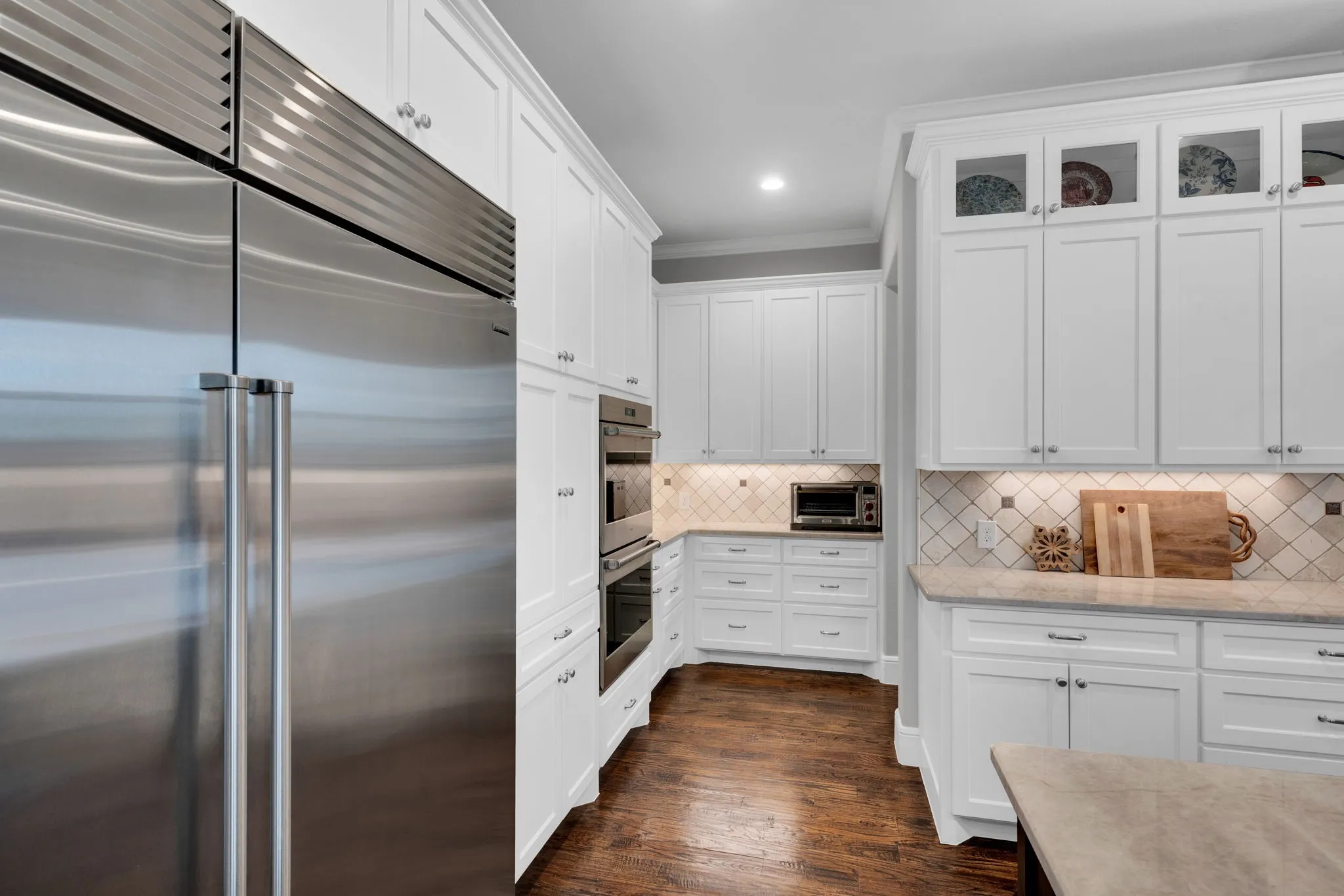 Kitchen featuring stainless steel appliances, white cabinets, decorative backsplash, light stone counters, and dark wood-style flooring