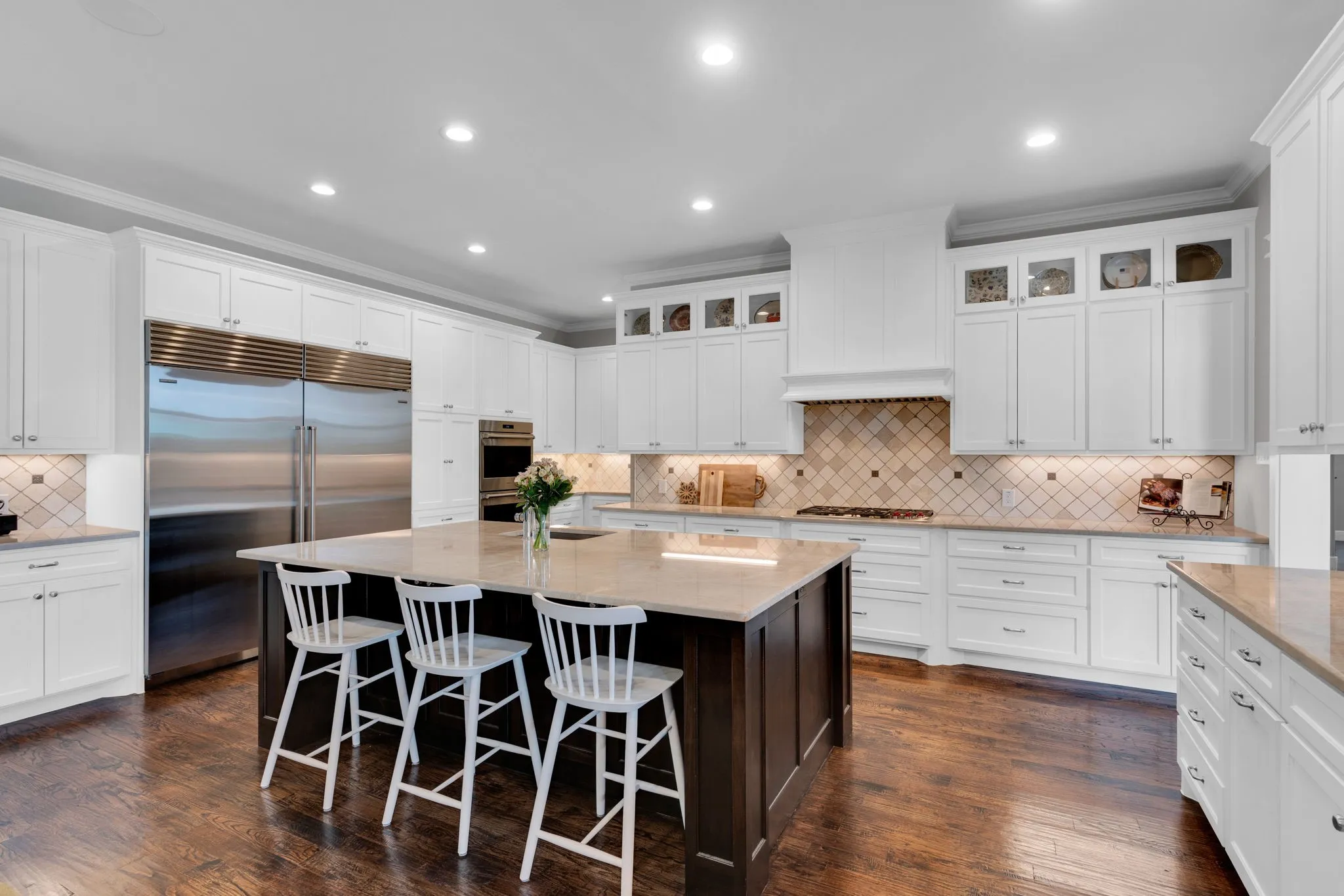 Kitchen featuring light stone countertops, decorative backsplash, appliances with stainless steel finishes, white cabinets, and ornamental molding