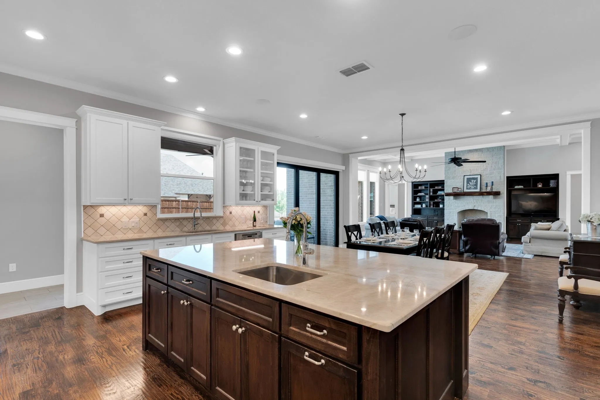 Kitchen with dark brown cabinetry, glass insert cabinets, white cabinets, light stone counters, and crown molding