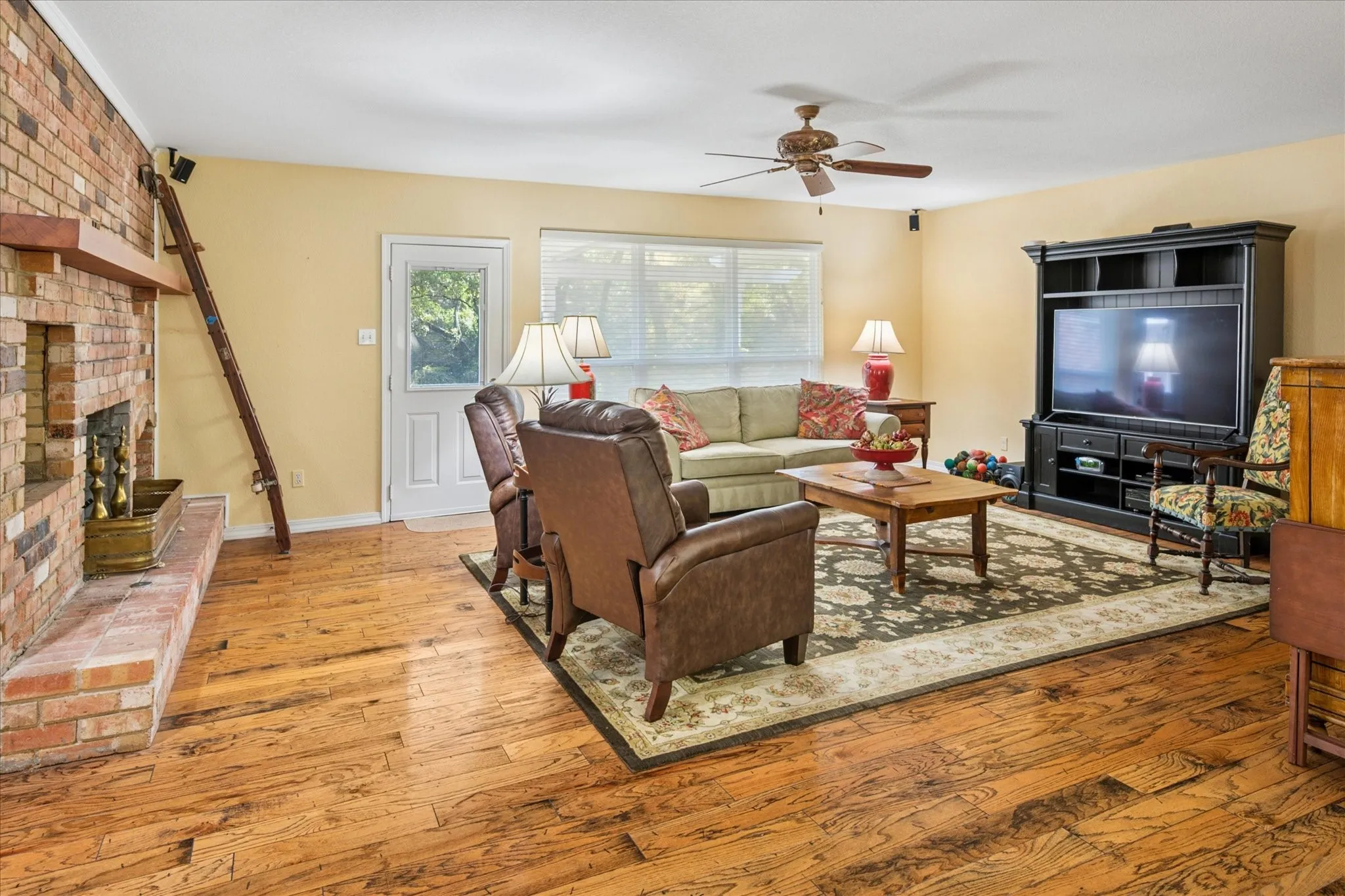 Living area featuring hardwood / wood-style floors, ceiling fan, and a brick fireplace