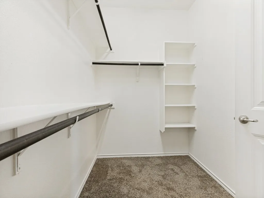 Spacious walk-in closet featuring white wire shelving, multiple hanging rods, and neutral-toned carpet flooring