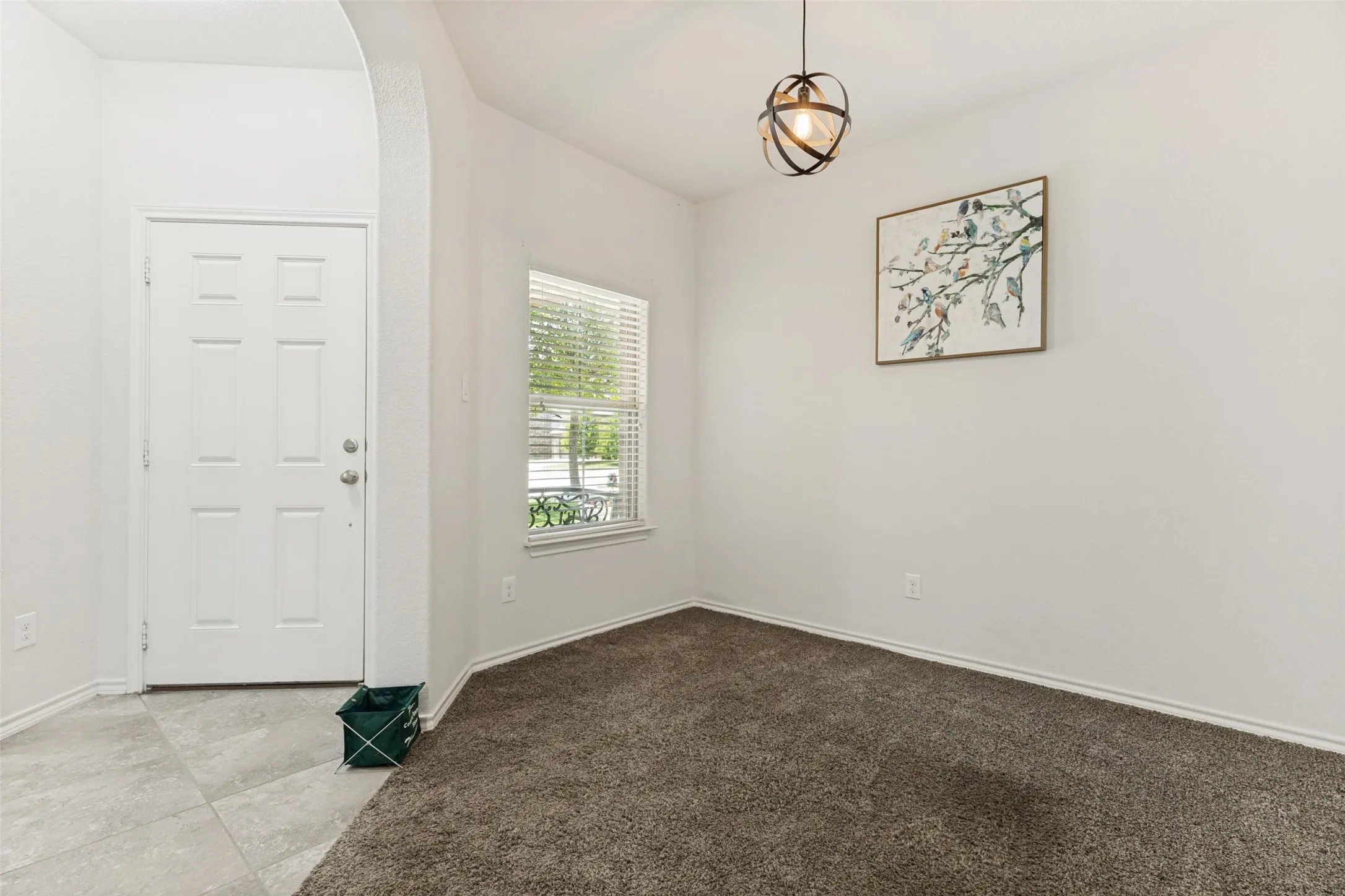 Entryway with light gray tile flooring, leading into a room featuring plush brown carpeting