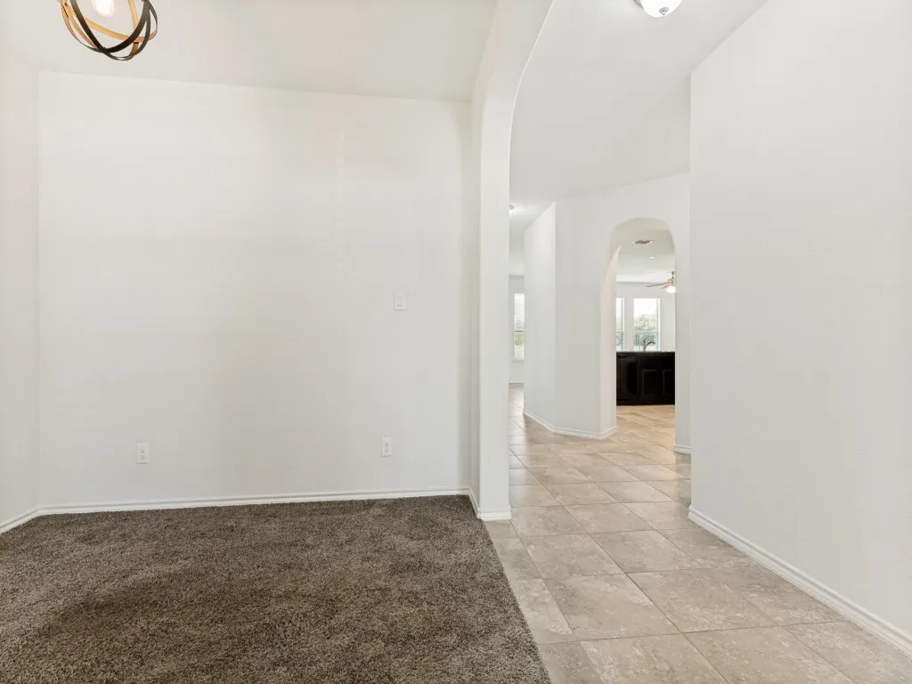 Arched doorways frame a tiled hallway with a view to a rear room, contrasting with a carpeted area featuring a contemporary ceiling light fixture