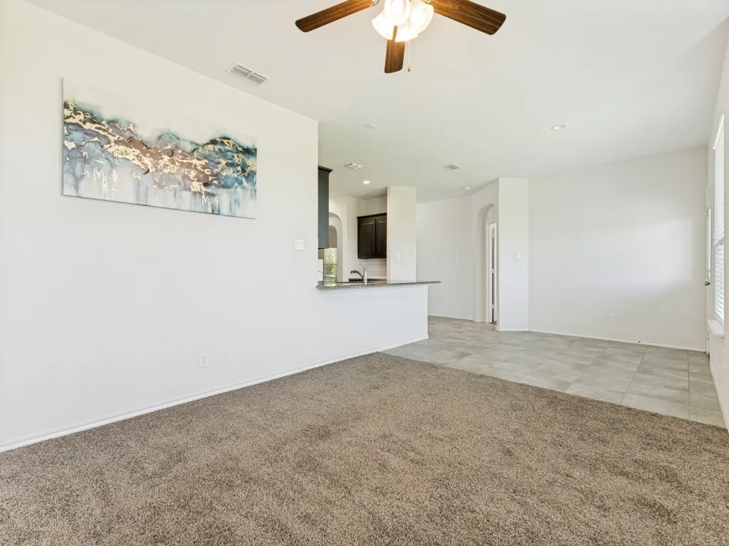 Spacious living area featuring neutral carpeting, a ceiling fan with integrated lighting, and white walls