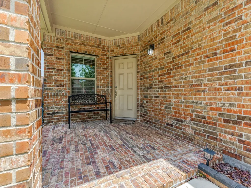 Covered entry featuring a brick exterior, coordinating brick flooring, and a recessed window with blinds