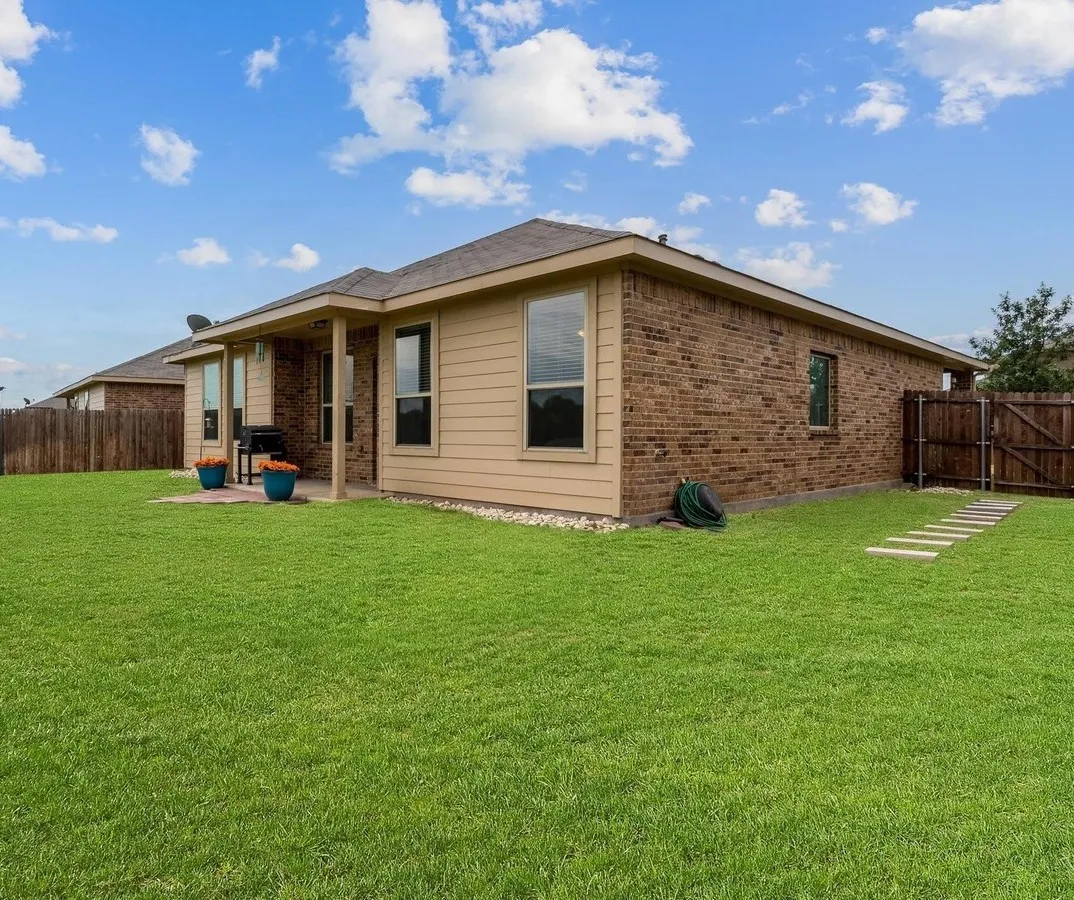 Expansive backyard featuring a lush lawn, a covered patio with concrete flooring, and a brick and siding exterior