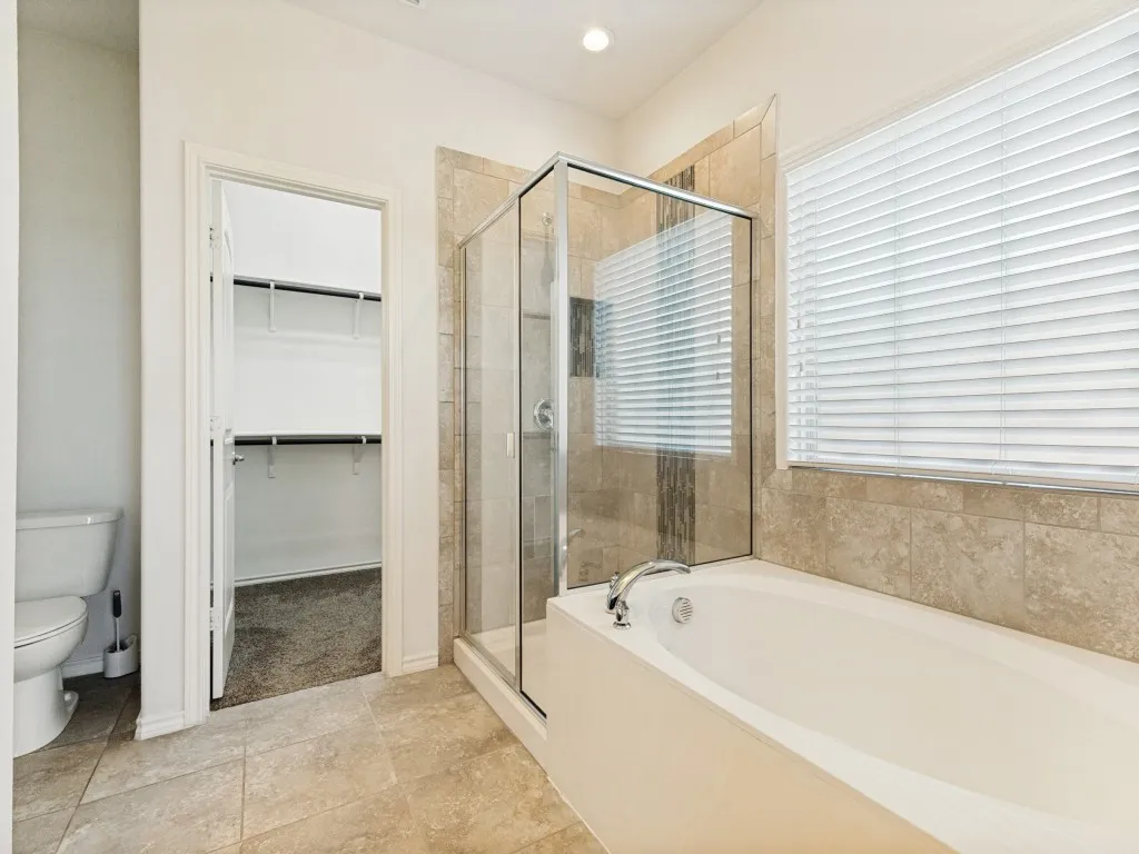 Soaking tub with a polished chrome faucet, adjacent to a glass-enclosed shower with tile surround