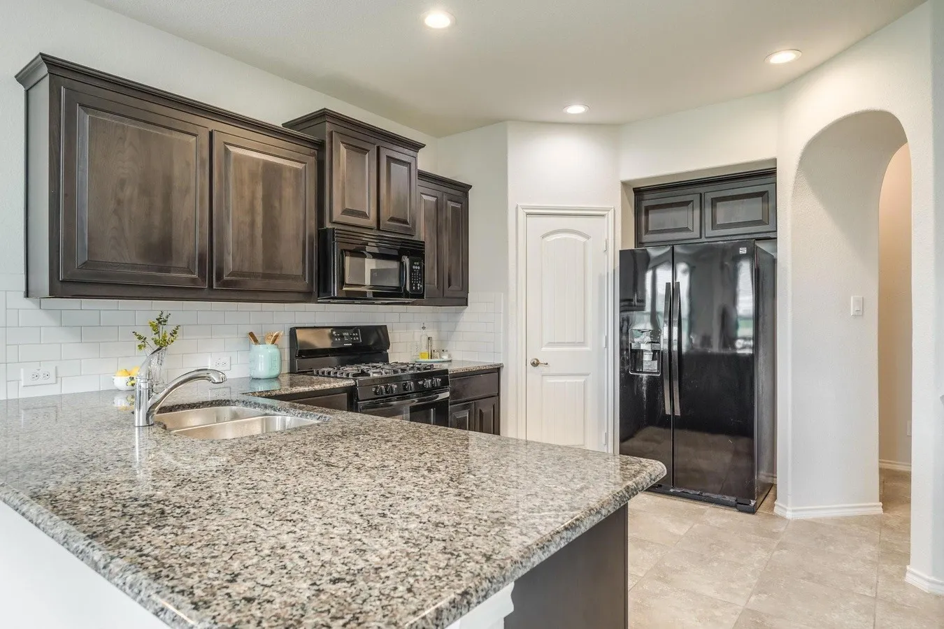 Kitchen featuring granite countertops, dark wood-finish cabinetry, subway tile backsplash, and stainless steel sink