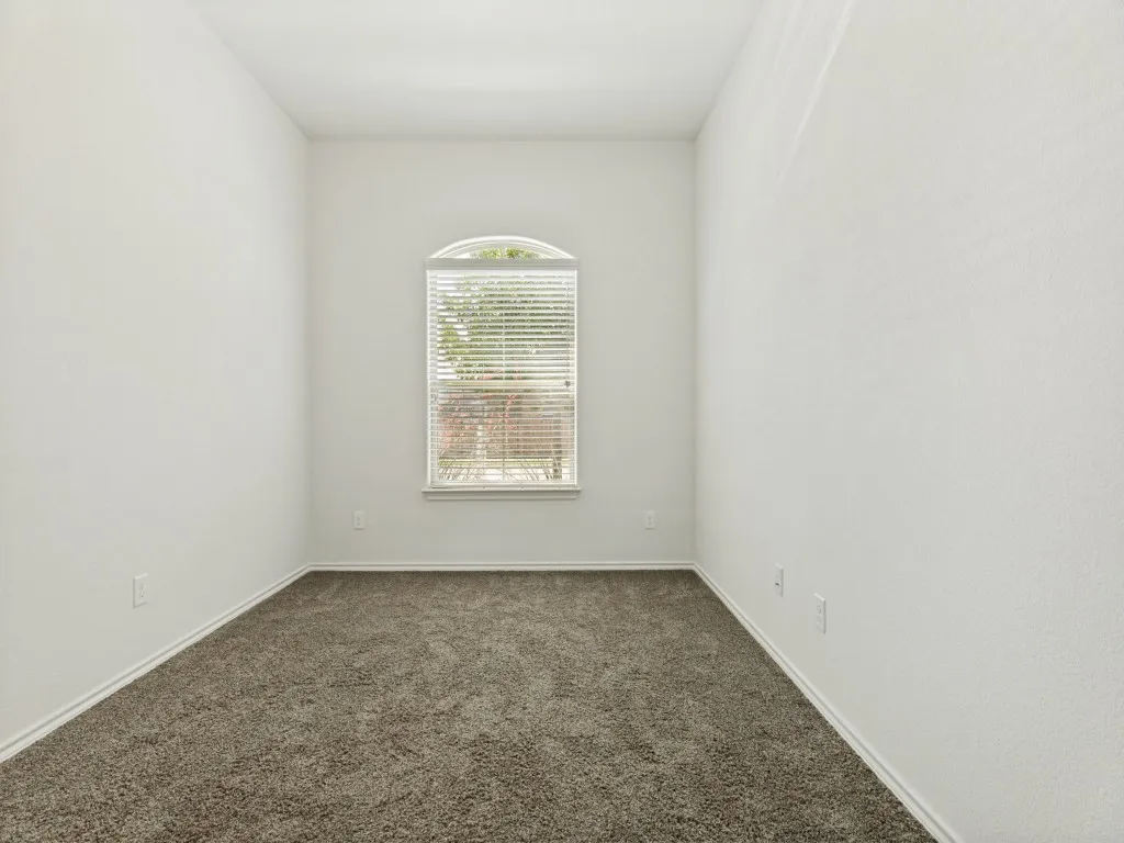 Arched window with blinds, carpet flooring, white baseboards, and neutral wall tones