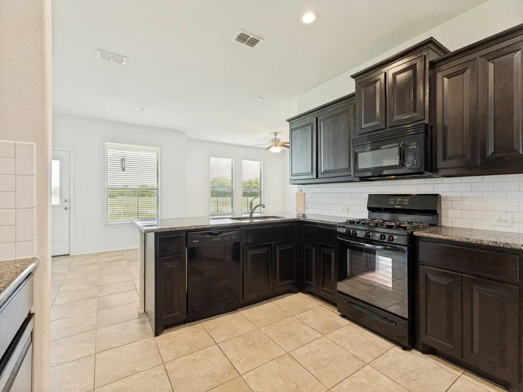 Kitchen featuring dark wood cabinetry, a subway tile backsplash, and black appliances