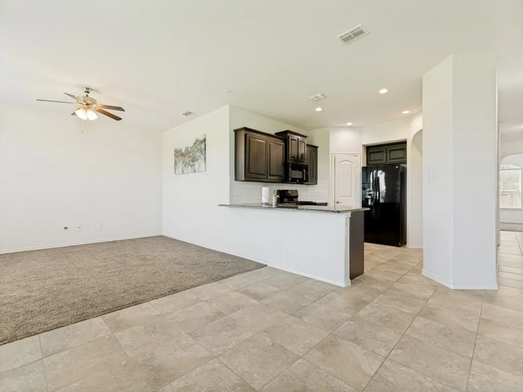 Open-concept kitchen and living area featuring dark wood-finish cabinetry, light-toned tiled flooring, and a breakfast bar with a light-colored countertop
