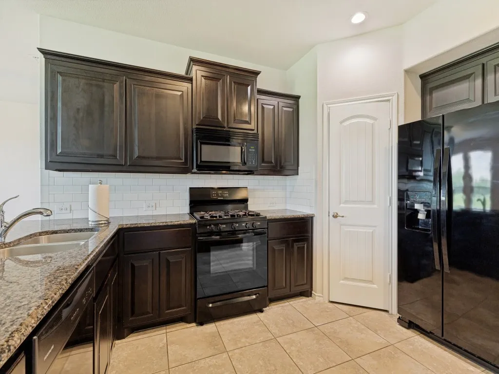 Kitchen featuring dark wood-finish cabinetry, light-toned granite countertops, and a subway tile backsplash