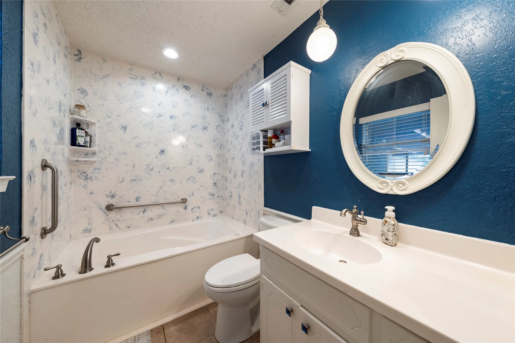 Bathroom featuring a textured wall, a bath, vanity, a textured ceiling, and light tile patterned floors