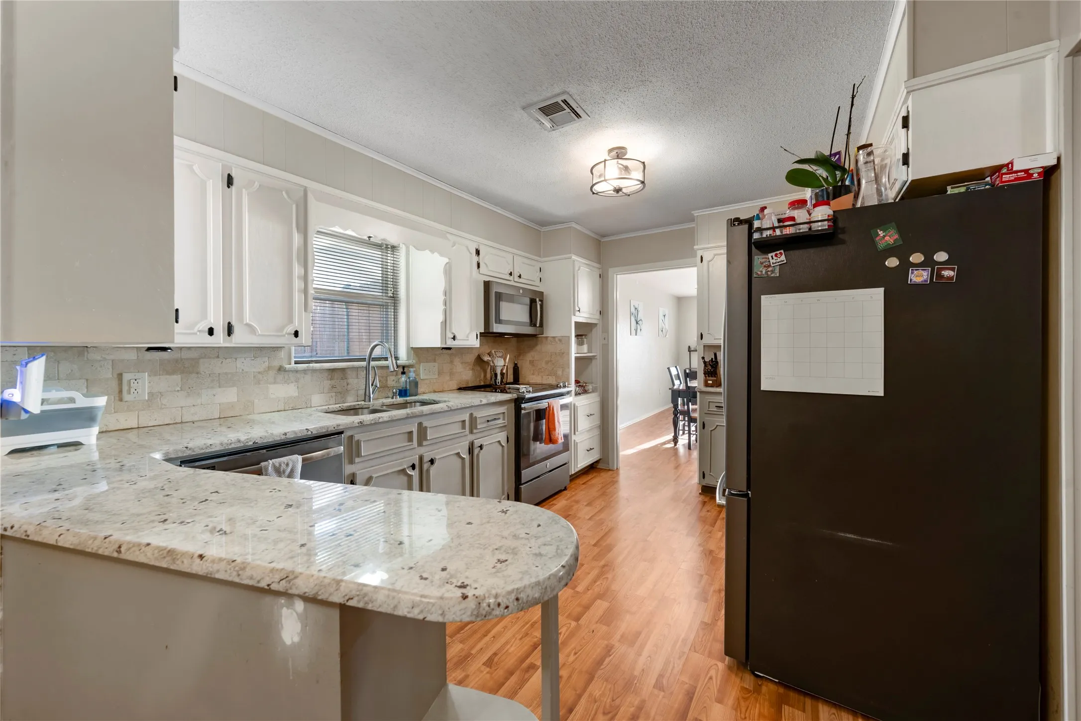 Kitchen featuring stainless steel appliances, crown molding, a peninsula, light wood-style flooring, and light stone counters