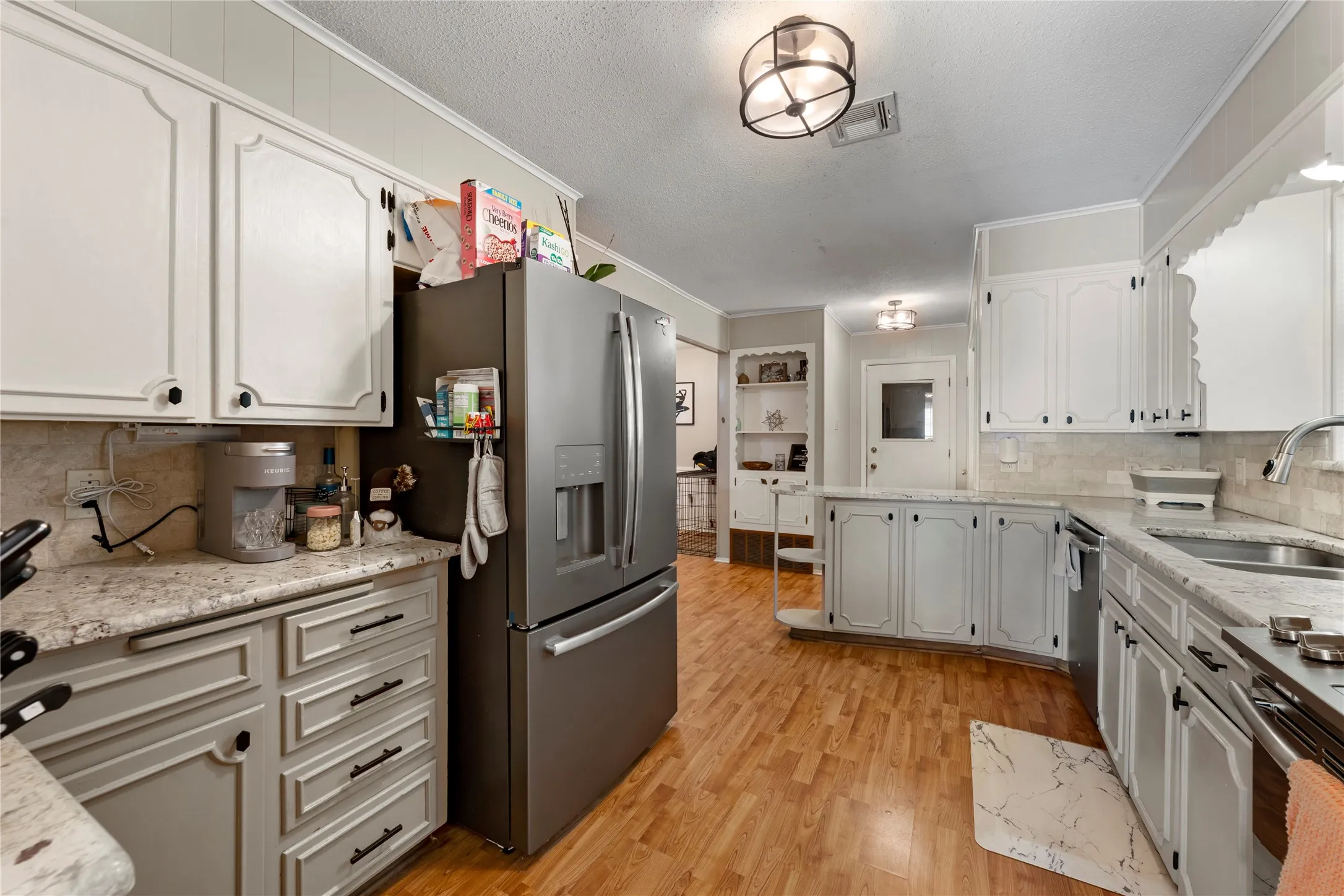 Kitchen featuring tasteful backsplash, light stone counters, crown molding, stainless steel appliances, and light wood finished floors