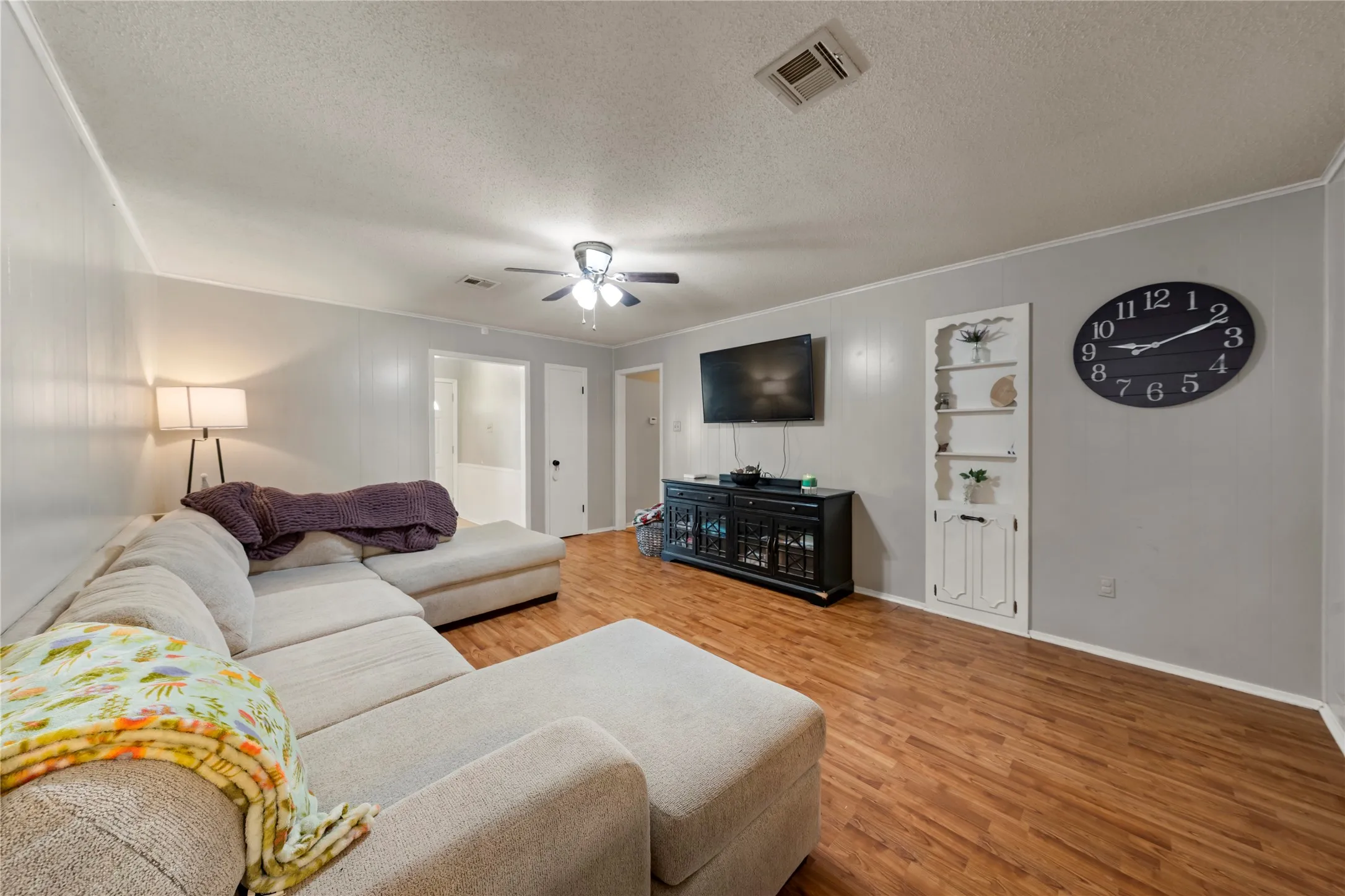 Living area featuring crown molding, light wood-style floors, a textured ceiling, and a ceiling fan