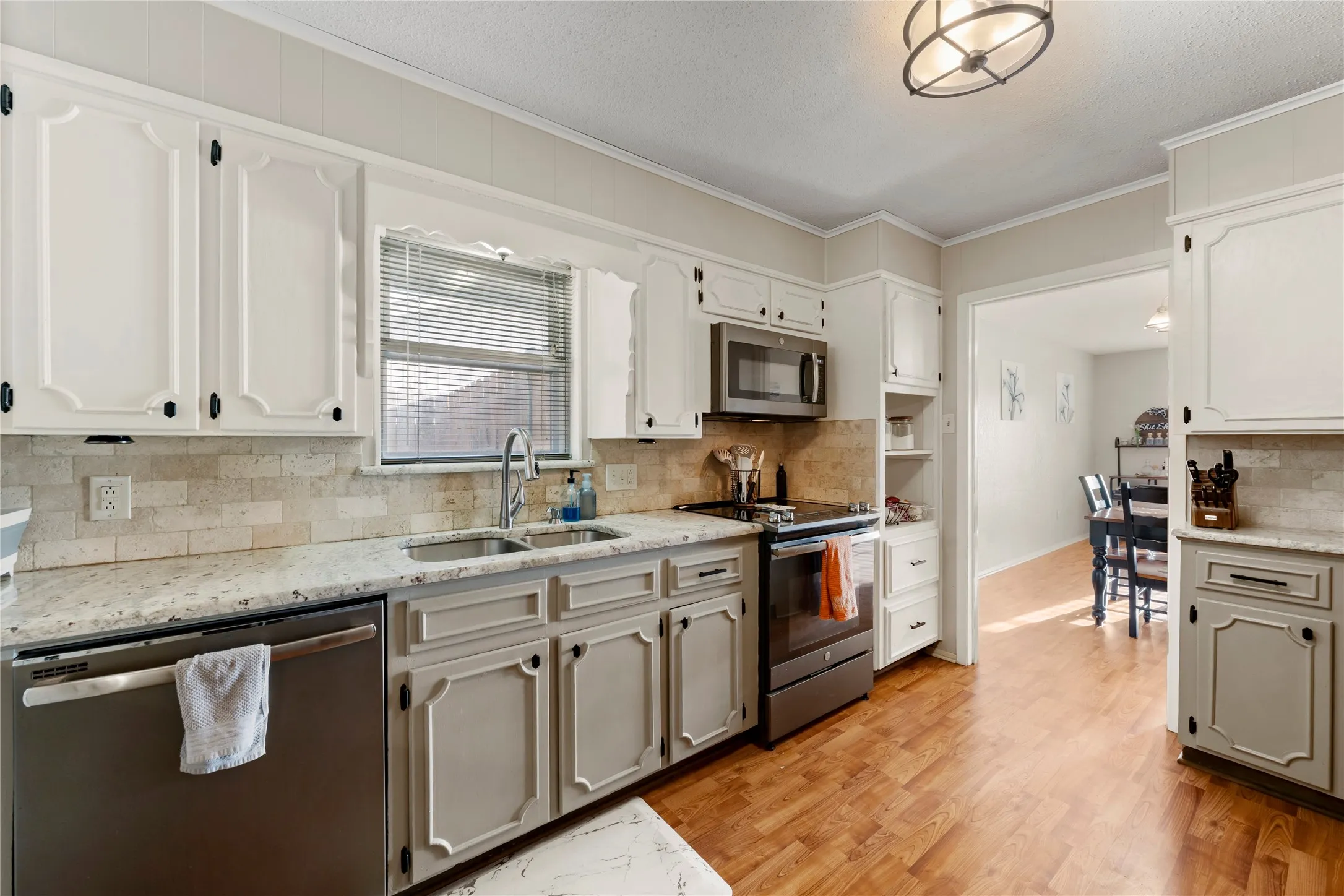 Kitchen with appliances with stainless steel finishes, decorative backsplash, crown molding, light wood-style floors, and light stone counters