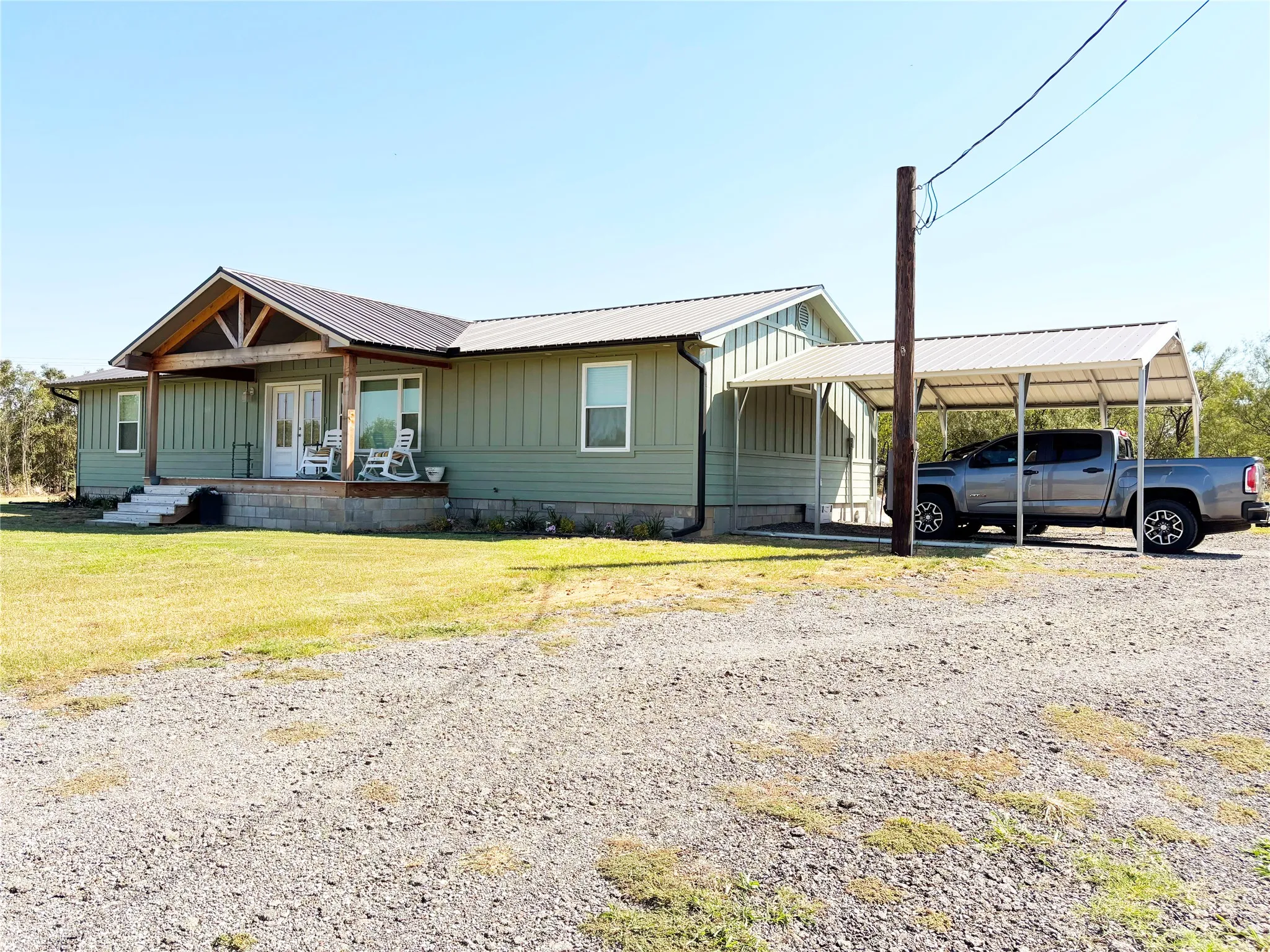 Side of home with covered porch, board and batten siding, a metal roof, a front lawn, and driveway