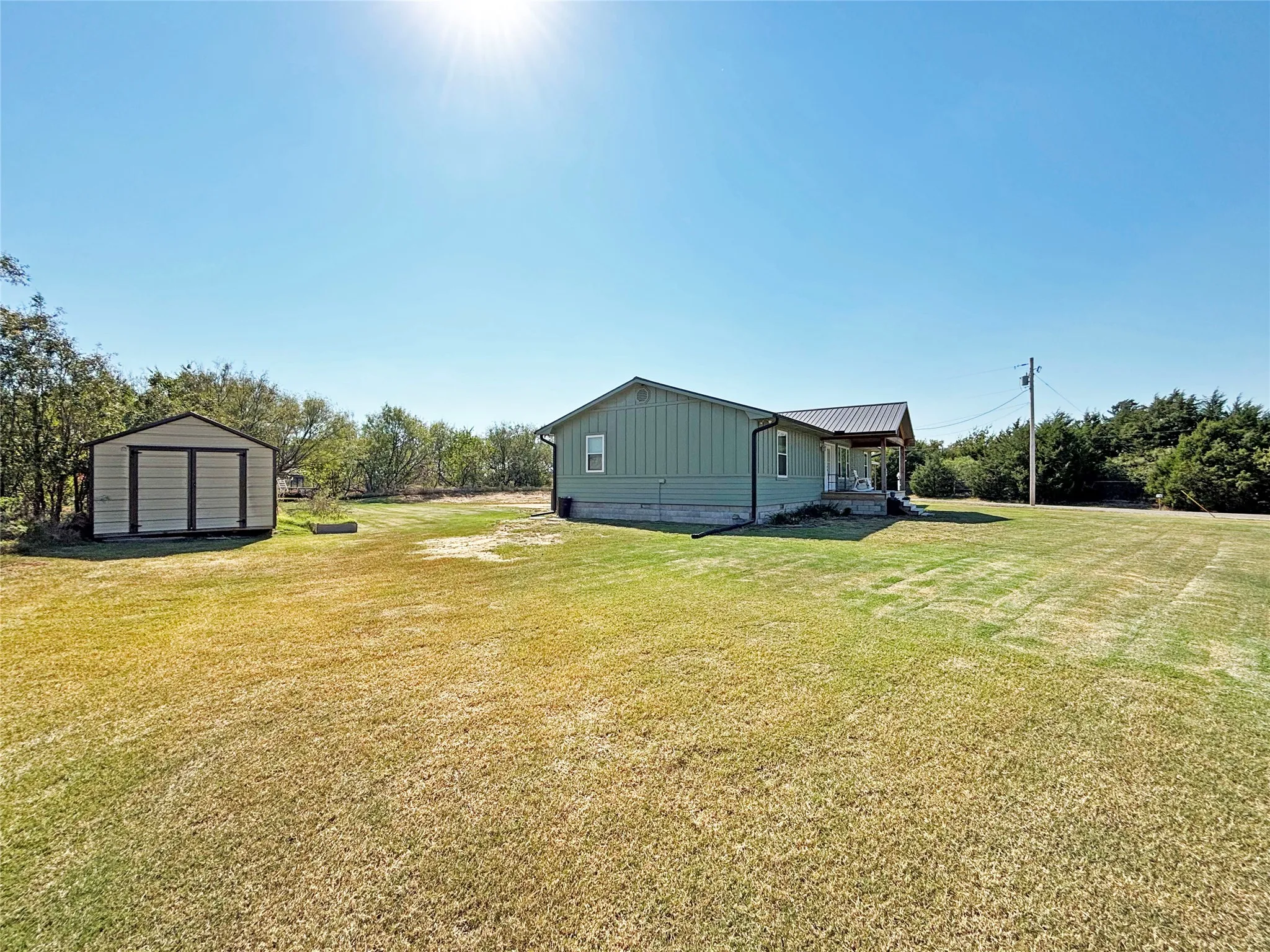 View of grassy yard featuring a storage shed, a porch, and view of scattered trees