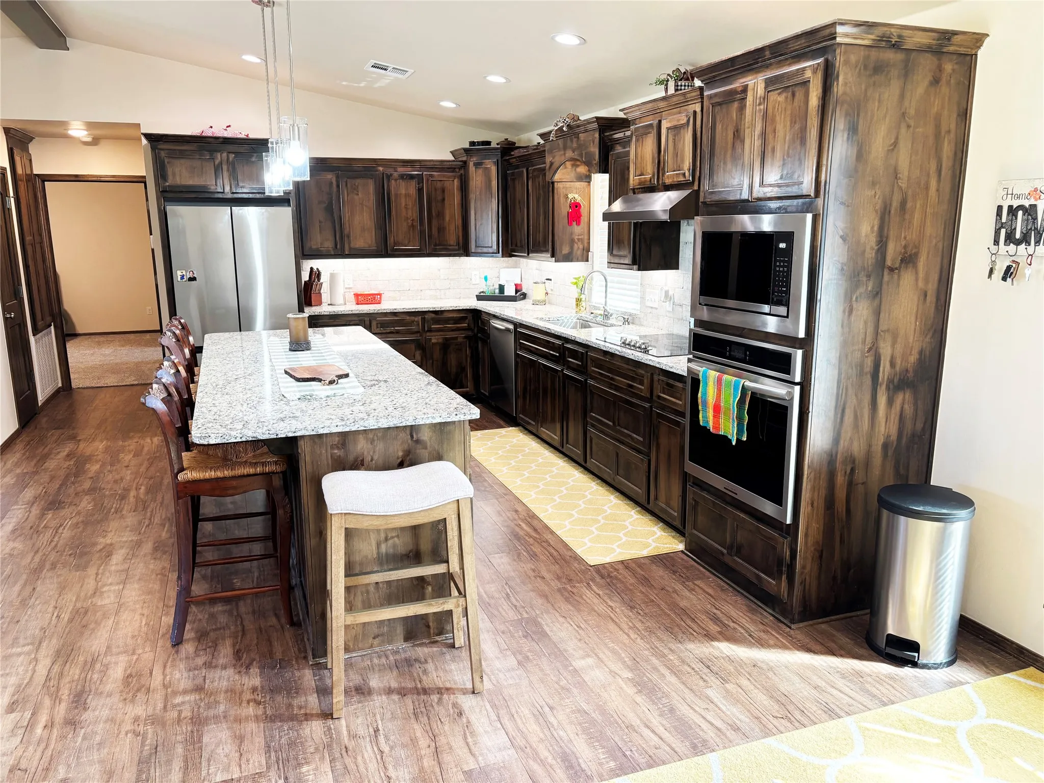 Kitchen with tasteful backsplash, light stone countertops, vaulted ceiling, a kitchen island, and dark brown cabinetry
