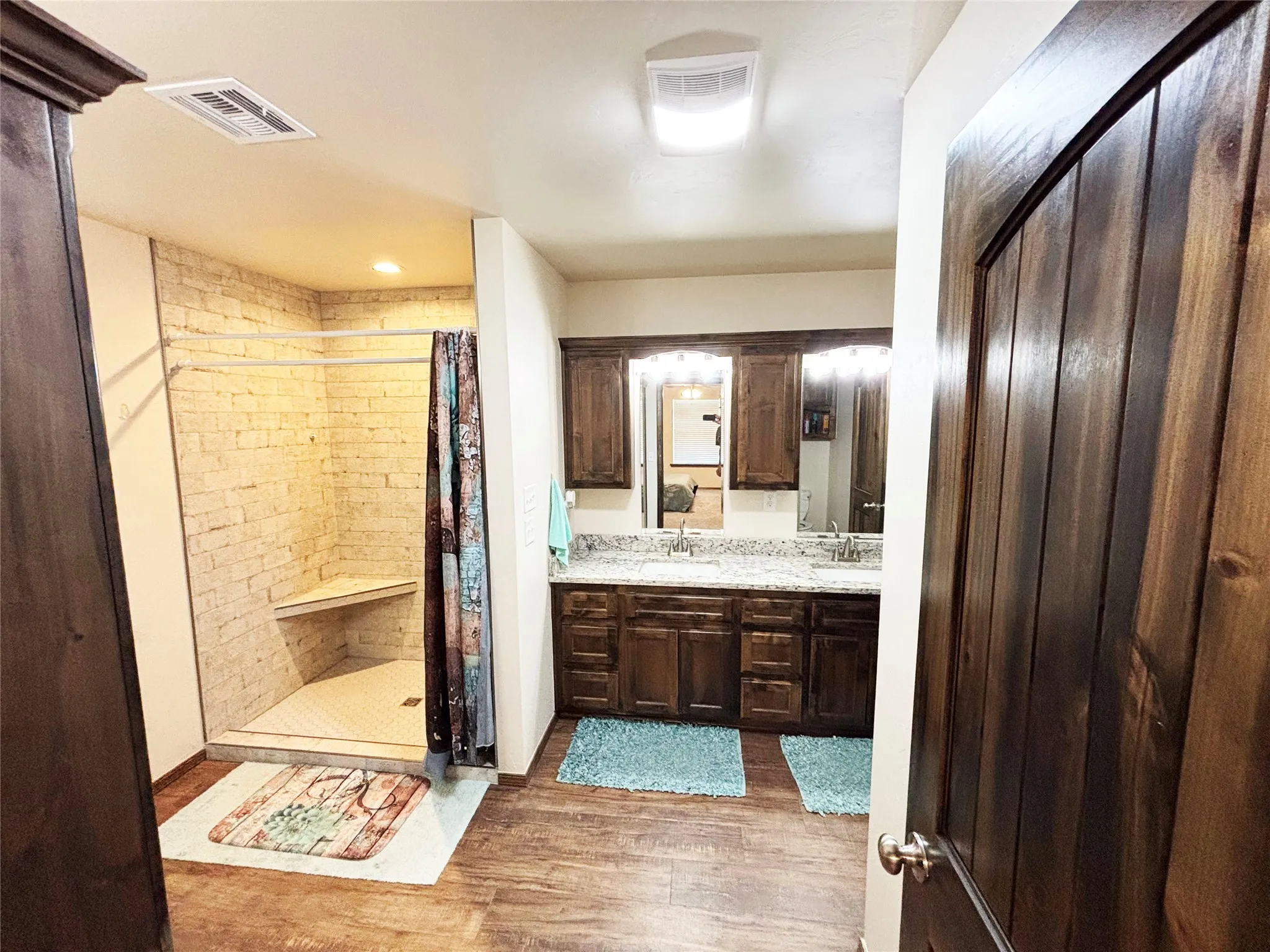 Bathroom with double vanity, light wood finished floors, and a stall shower