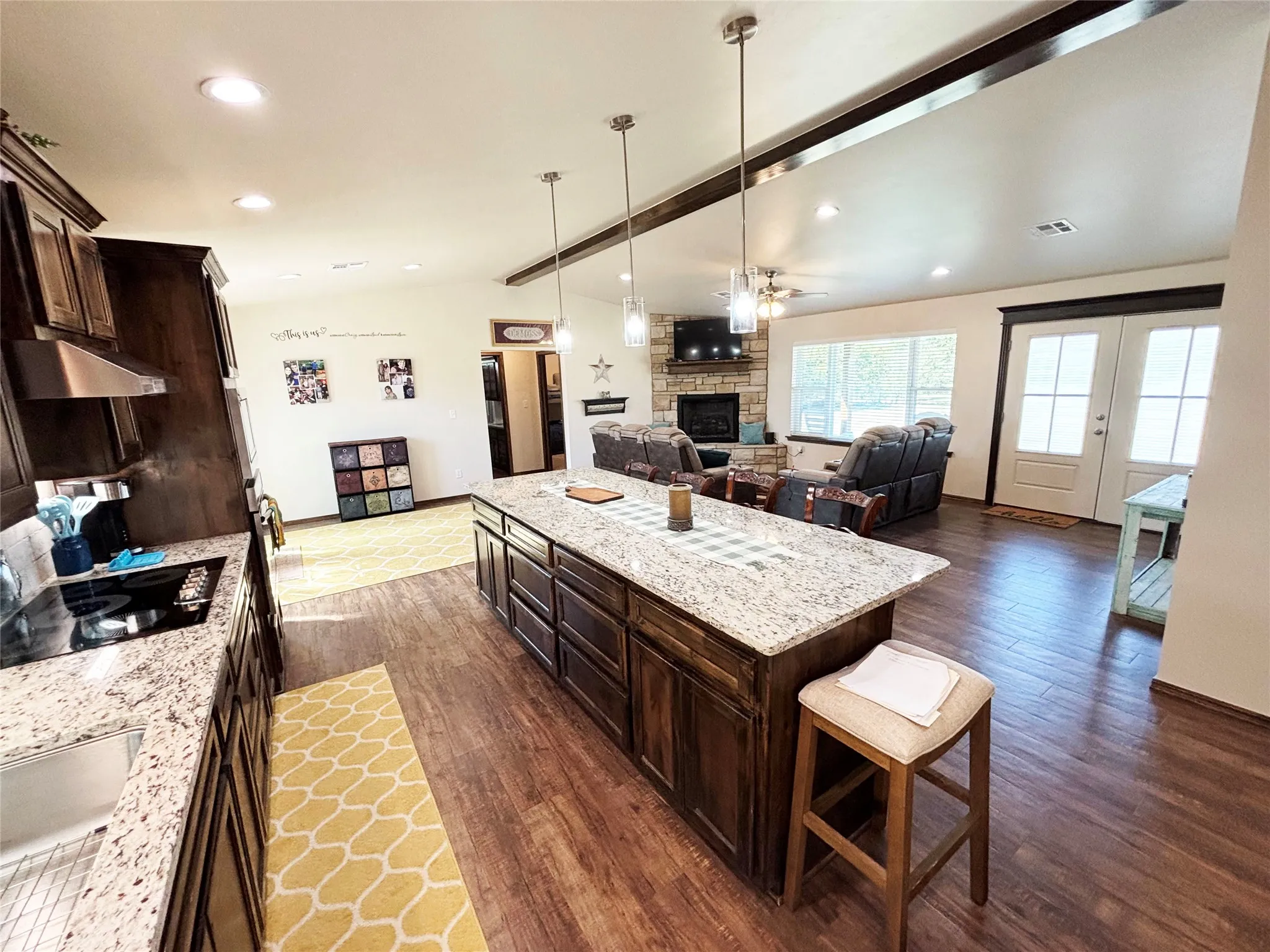 Kitchen featuring dark brown cabinets, light stone countertops, a stone fireplace, a kitchen breakfast bar, and decorative light fixtures