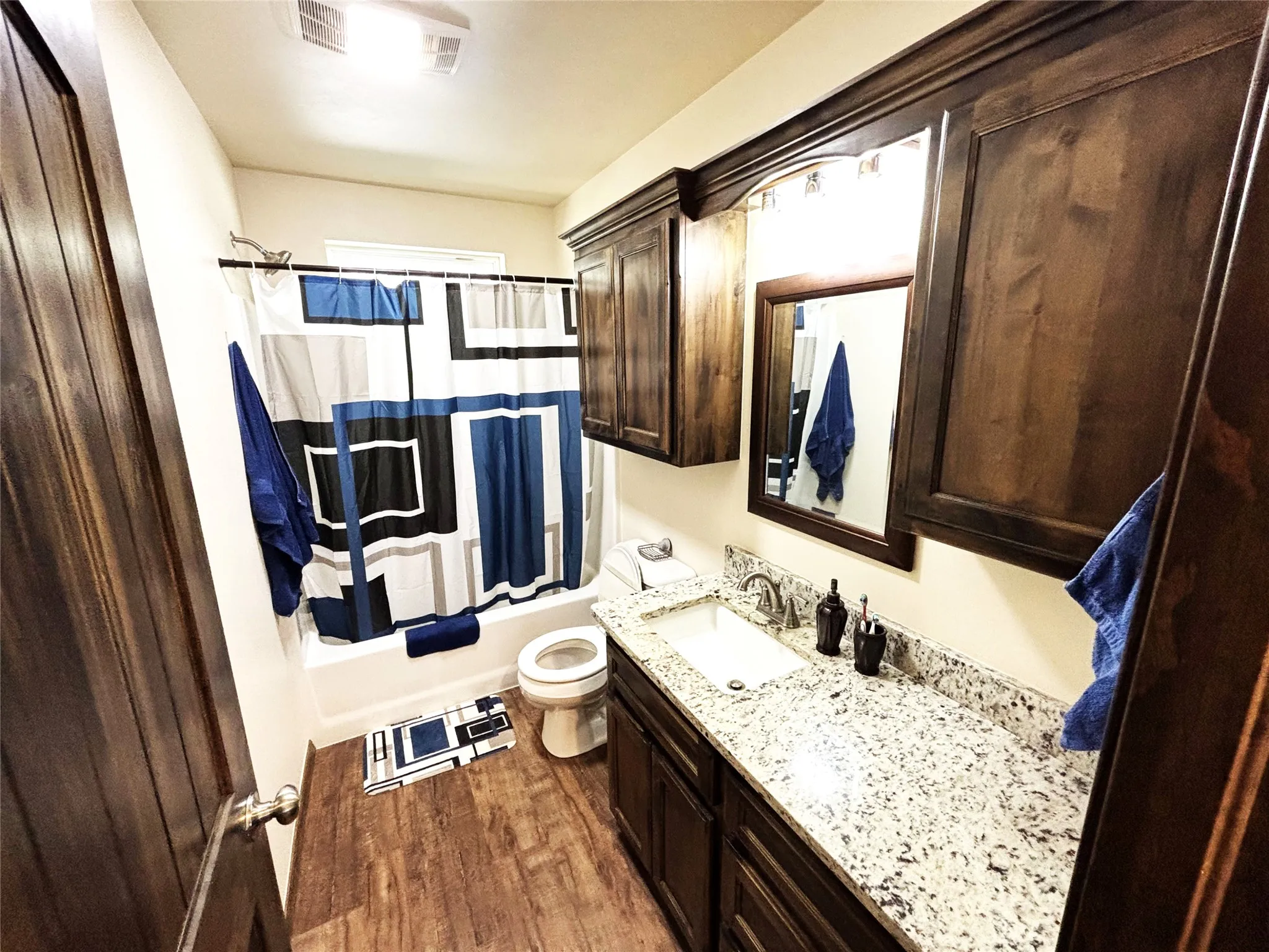 Bathroom with luxury vinyl plank flooring, shower / bathtub combination with curtain, and vanity