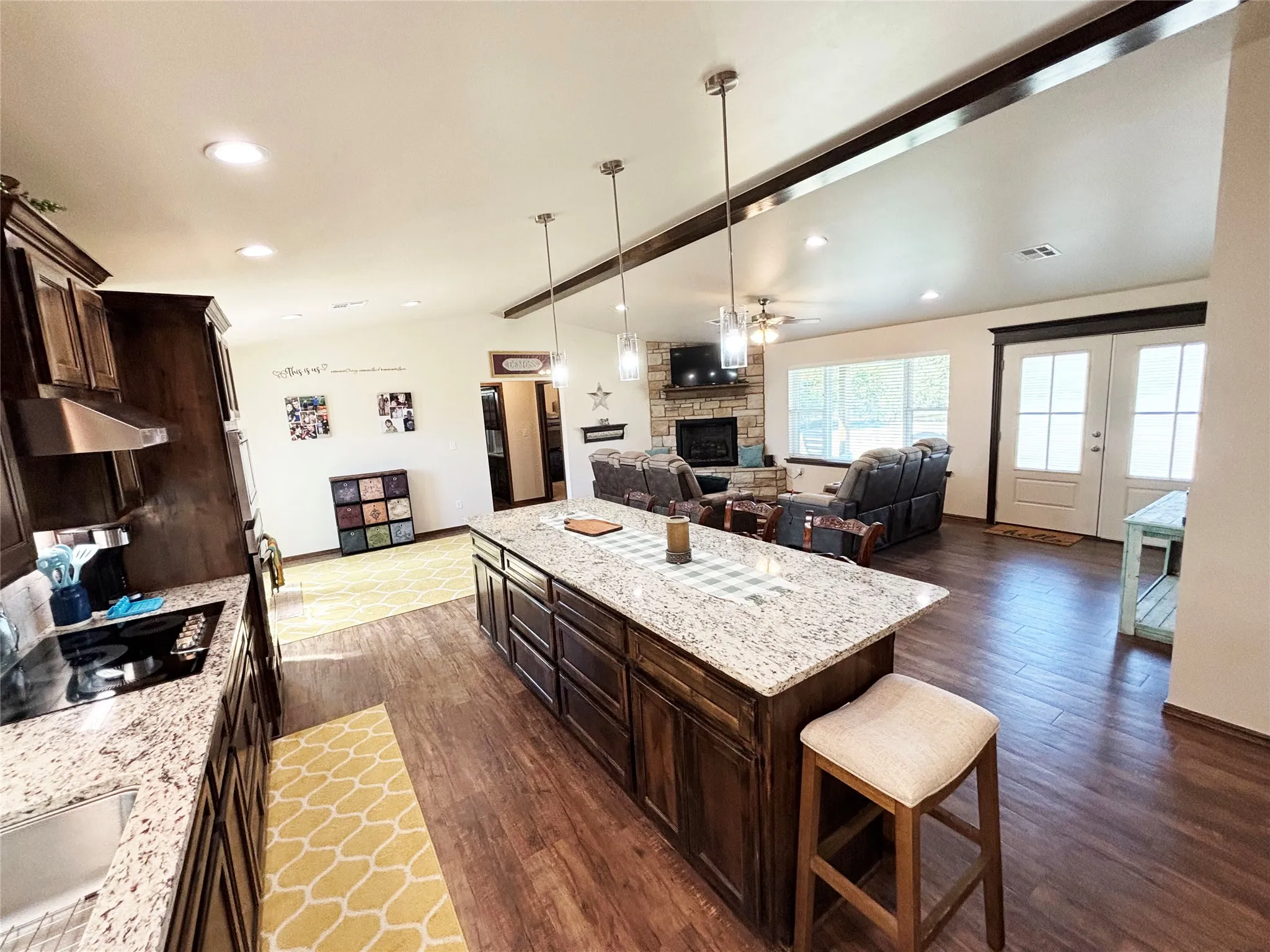 Kitchen featuring dark brown cabinets, light stone counters, a breakfast bar, open floor plan, and decorative light fixtures