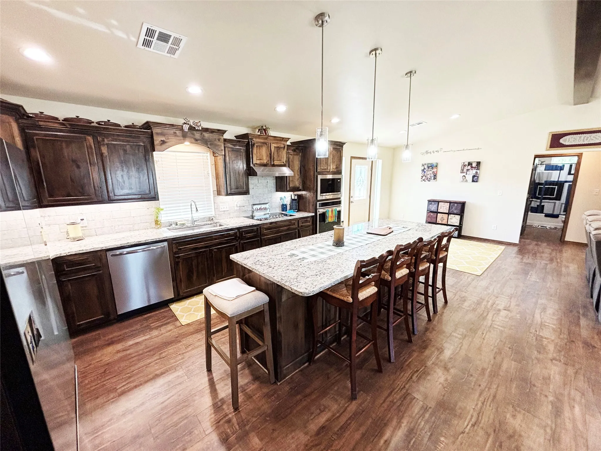 Kitchen featuring dark brown cabinetry, decorative backsplash, pendant lighting, a breakfast bar area, and light stone countertops