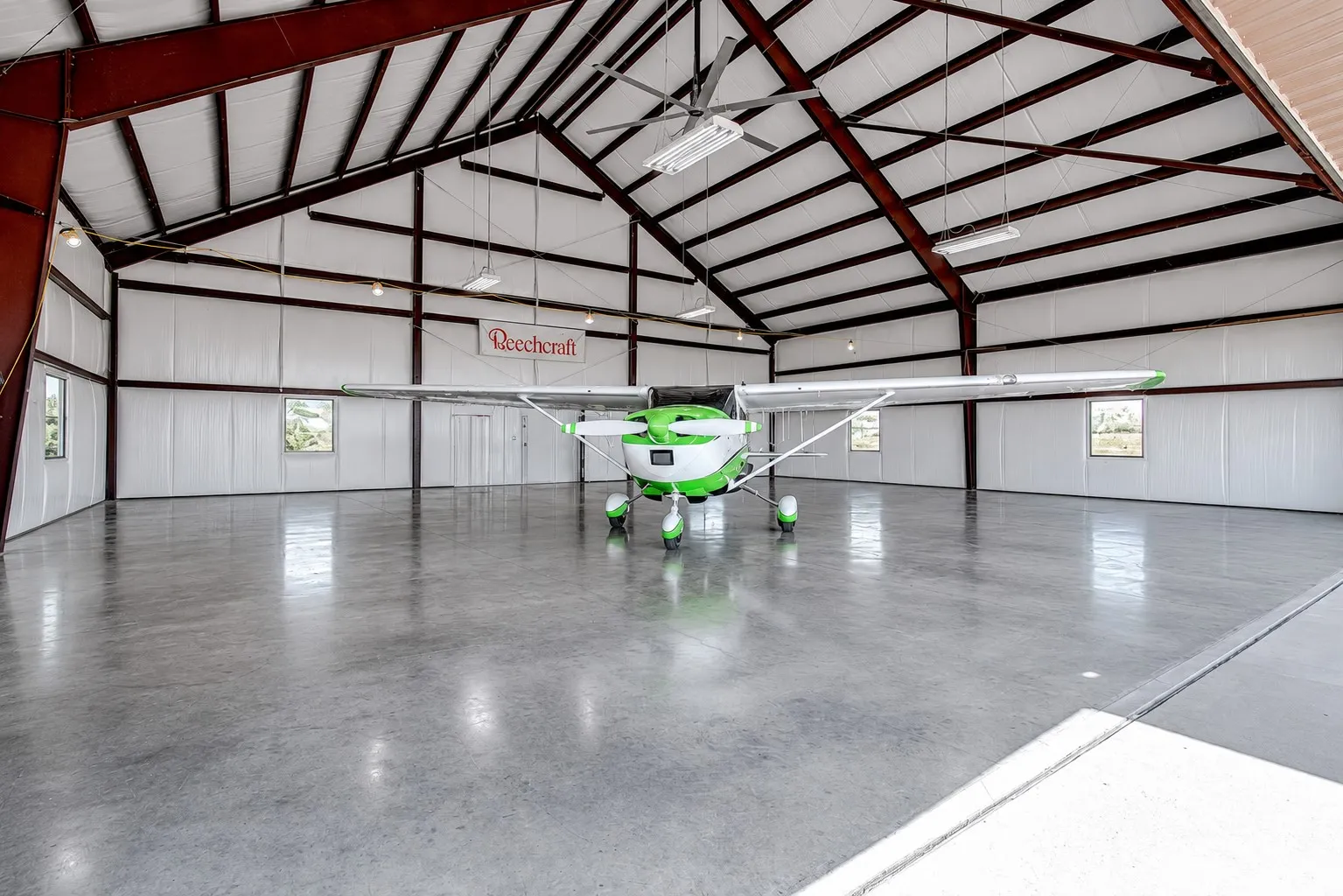 Expansive hangar with a high vaulted ceiling, exposed structural beams, polished concrete flooring, multiple windows, and suspended lighting fixtures - Cleaned with AI