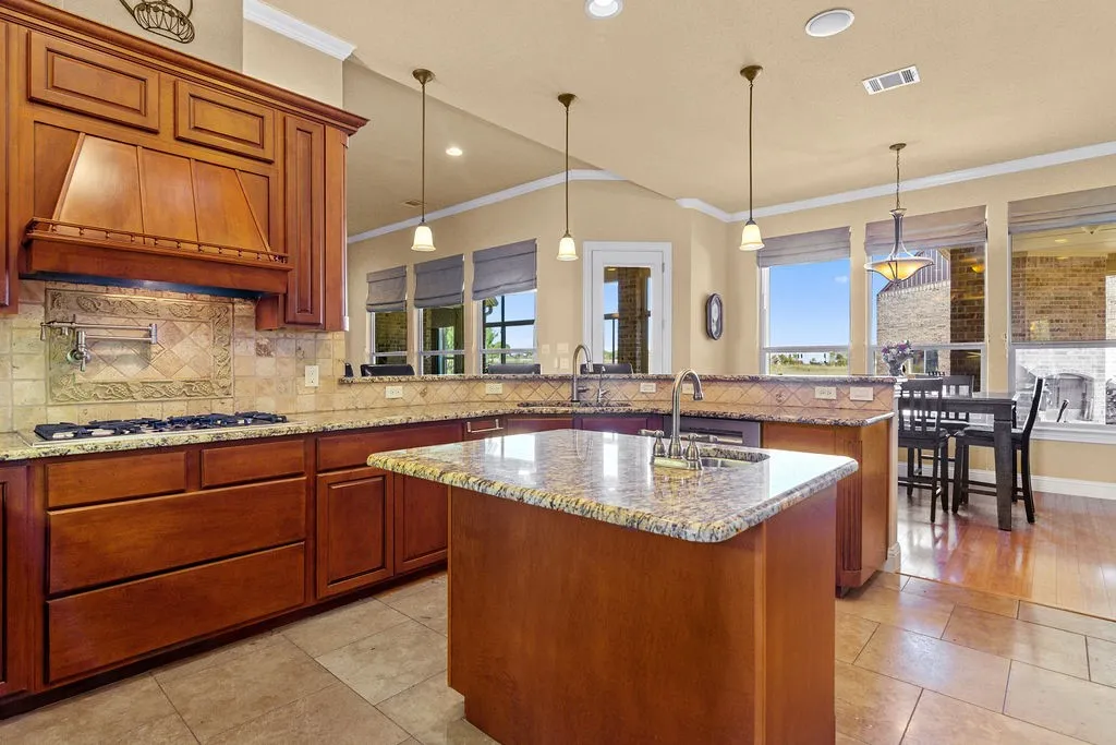 Kitchen with brown cabinets, pendant lighting, ornamental molding, a peninsula, and light stone counters
