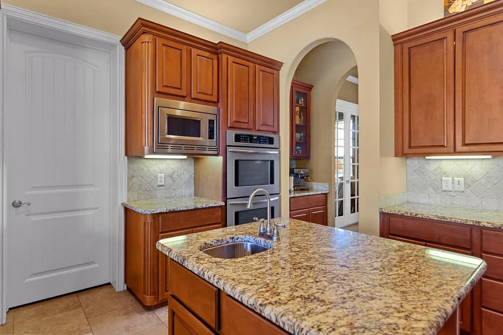Kitchen featuring decorative backsplash, arched walkways, appliances with stainless steel finishes, crown molding, and light stone counters
