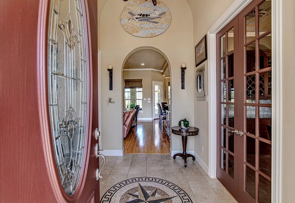 Foyer entrance with arched walkways, crown molding, light tile patterned floors, inlaid floor details, and french doors