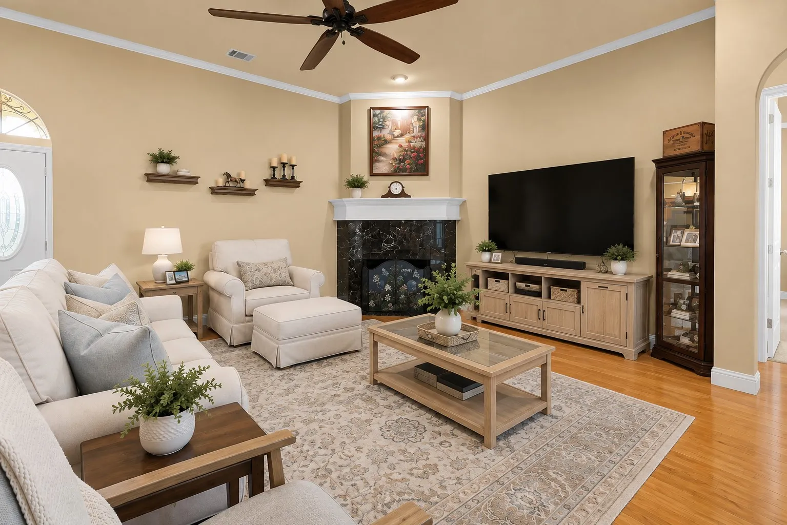 Wood-finish flooring, corner fireplace with a dark stone surround and white mantel, overhead ceiling fan, and decorative crown molding