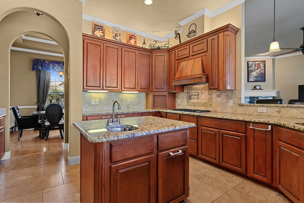 Kitchen featuring pendant lighting, light stone countertops, a center island with sink, backsplash, and ornamental molding