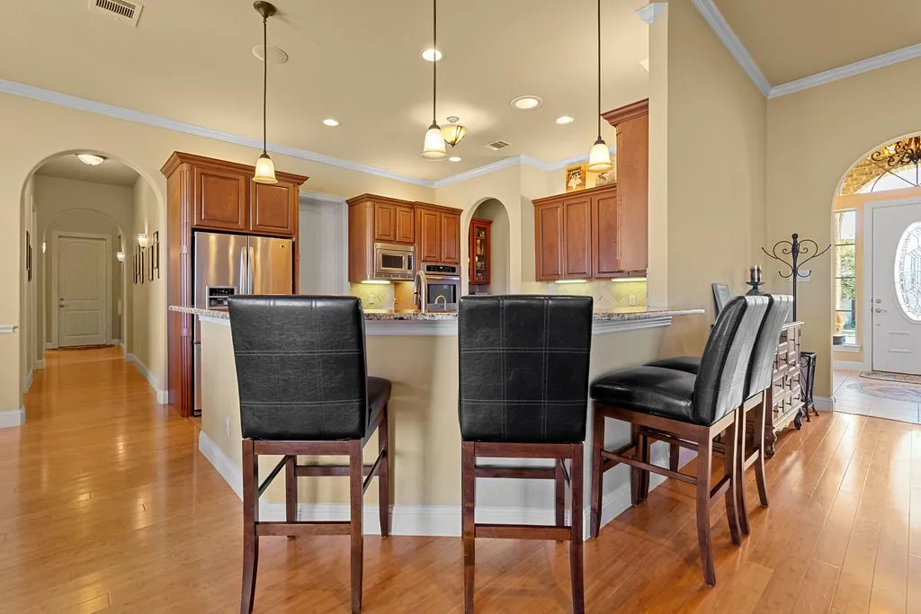 Kitchen featuring arched walkways, a kitchen breakfast bar, tasteful backsplash, decorative light fixtures, and ornamental molding