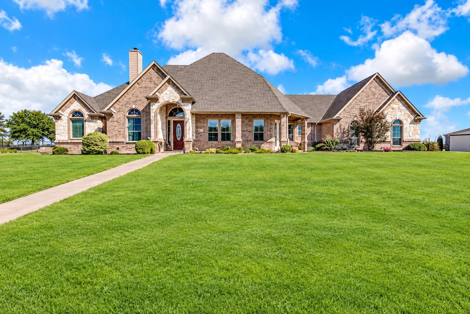 Brick and stone exterior with arched windows, a covered entry, an attached garage, and an expansive lawn