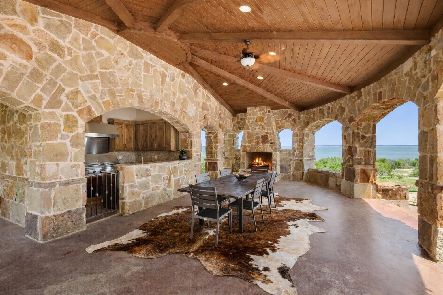 Stone-clad outdoor living area featuring a vaulted wood-plank ceiling, stone fireplace, and built-in outdoor kitchen with stainless steel appliances