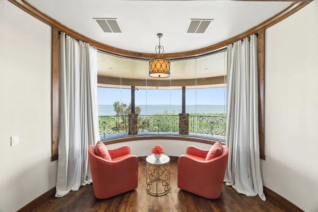 Curved window wall with expansive outdoor scenery, detailed wrought iron railing, rich wood-finish flooring, and a decorative chandelier