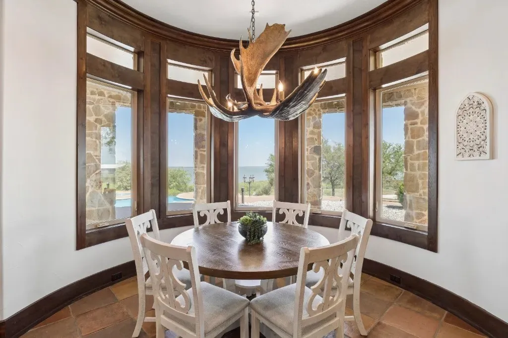 Curved window wall with dark wood trim, stone exterior accents visible through windows, and a sculptural antler-style chandelier