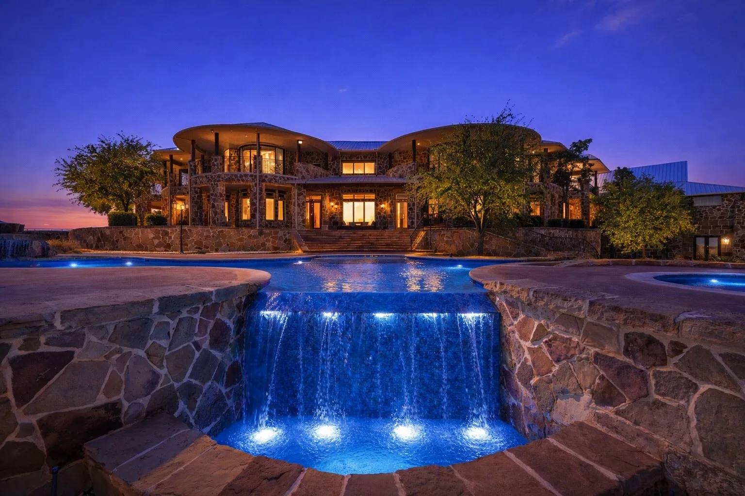 Expansive multi-level stone residence featuring a large water feature with integrated lighting, multiple swimming pools, and a stone patio