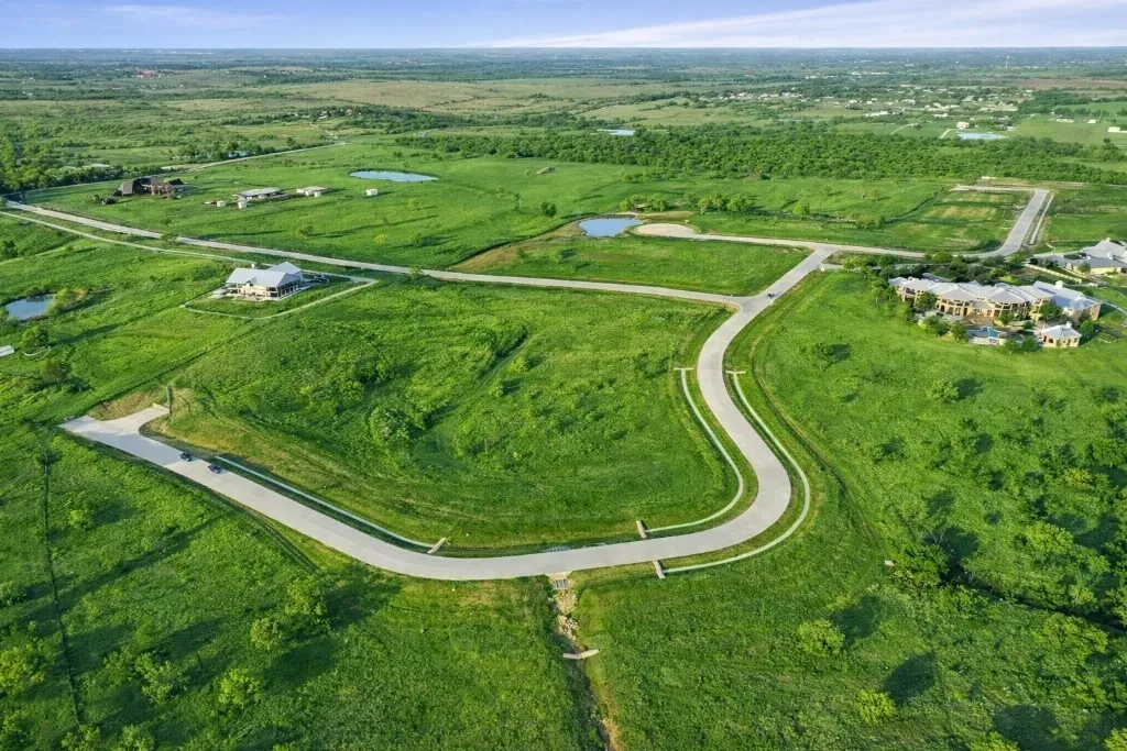 Expansive undeveloped land parcels featuring a winding paved road and scattered established homes